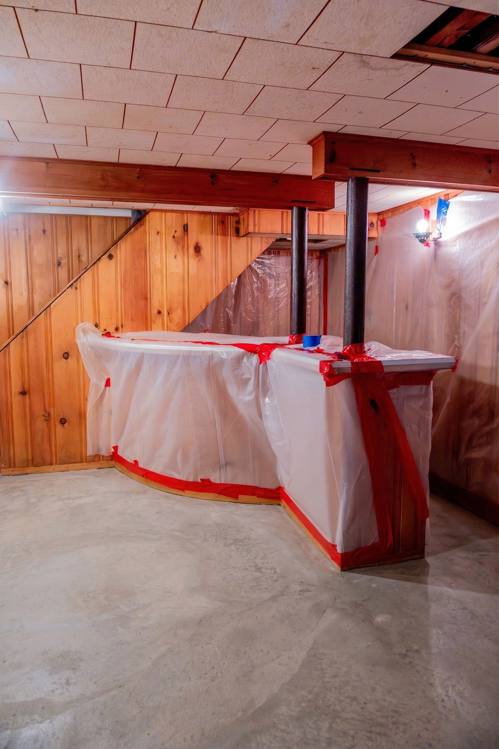 Basement room with a plastic-covered table wrapped in red tape and wood-paneled walls