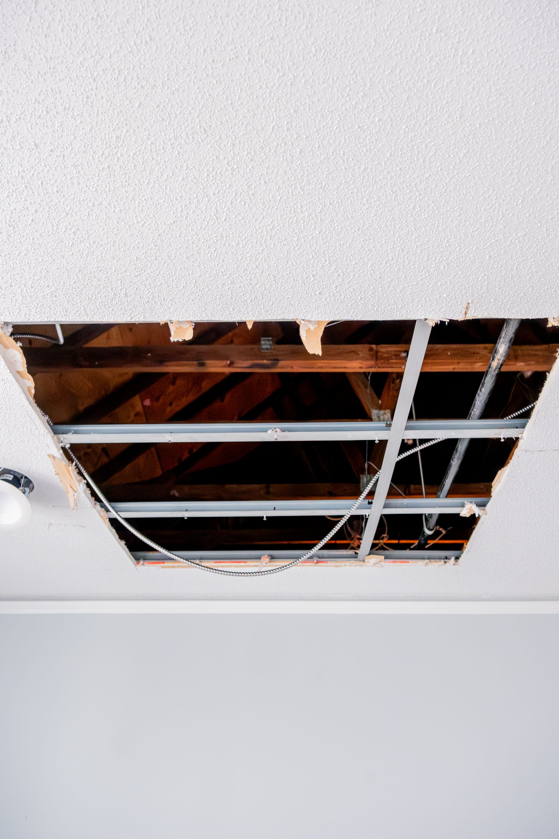 Ceiling with a large damaged section exposing wooden beams and metal framing.