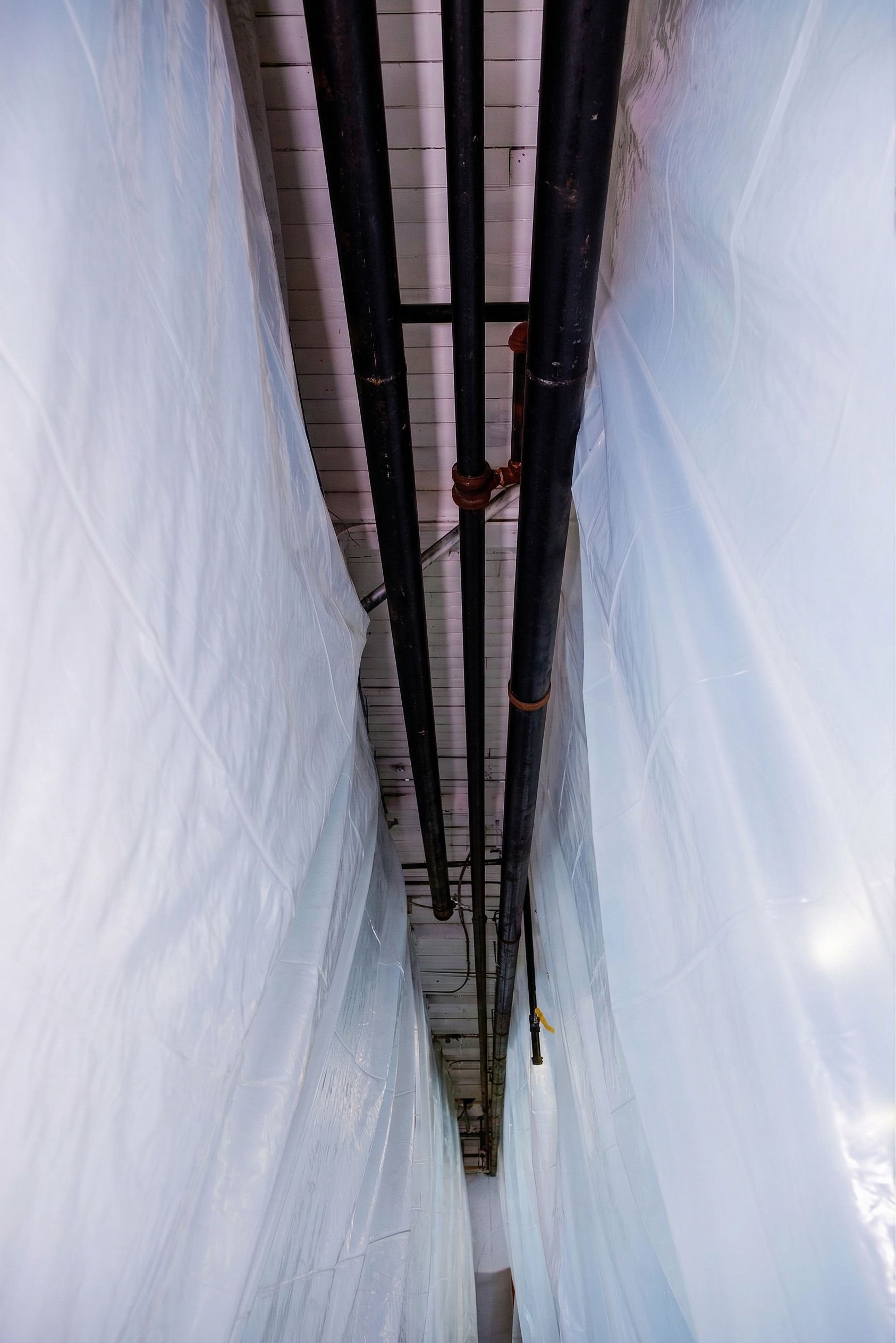 Narrow alleyway between white plastic-covered walls with pipes running overhead
