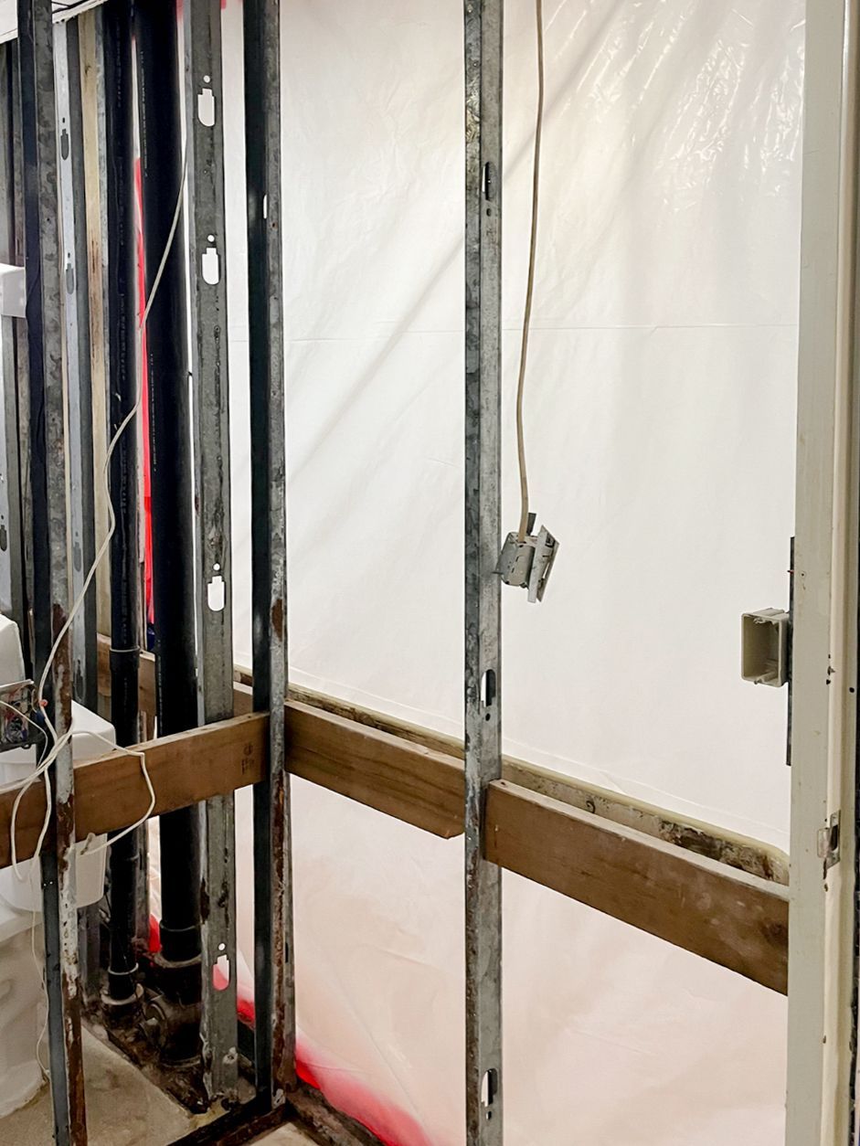 Exposed wall framing with metal studs and white plastic sheeting in a construction area