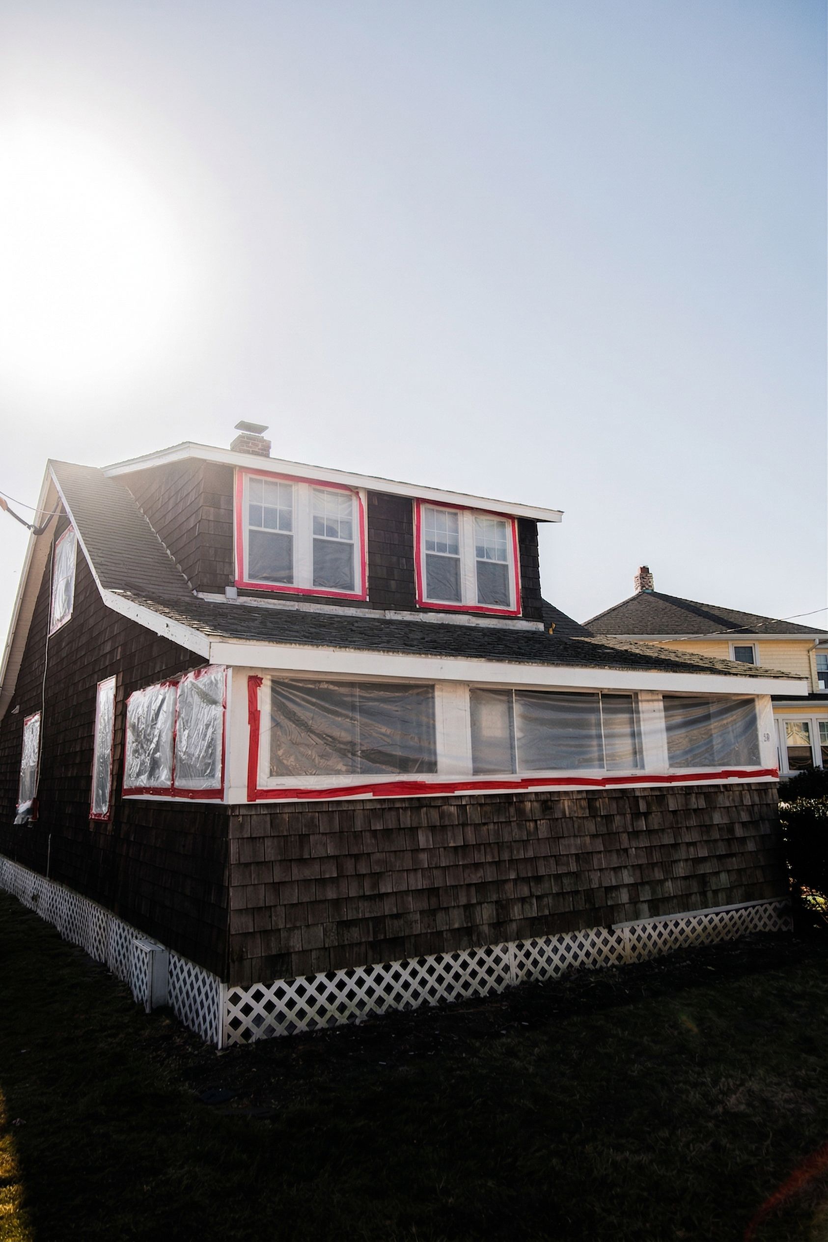 Small house with red-trimmed windows and a dark shingled roof under bright sunlight.