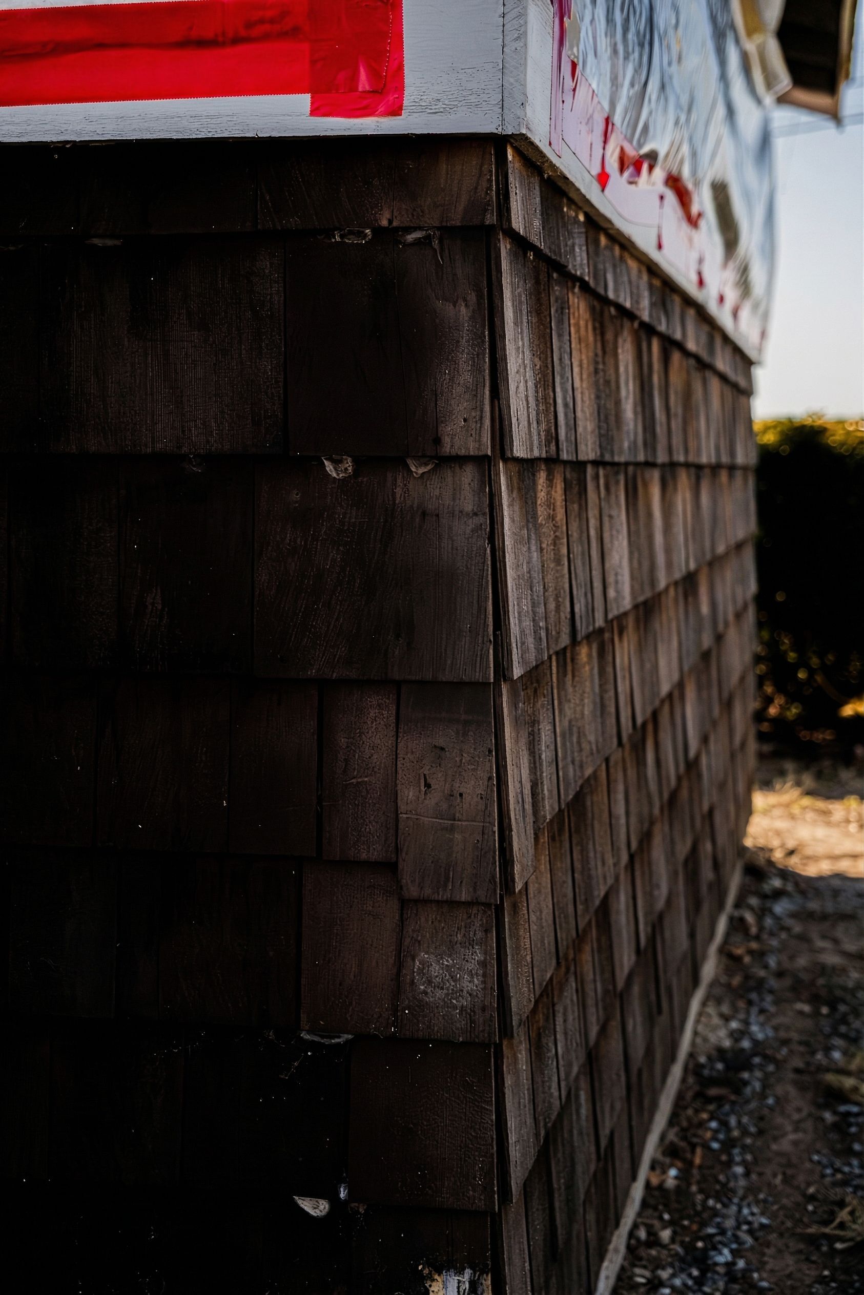 Close-up of a building corner with dark wooden shingles and a red trim at the top.