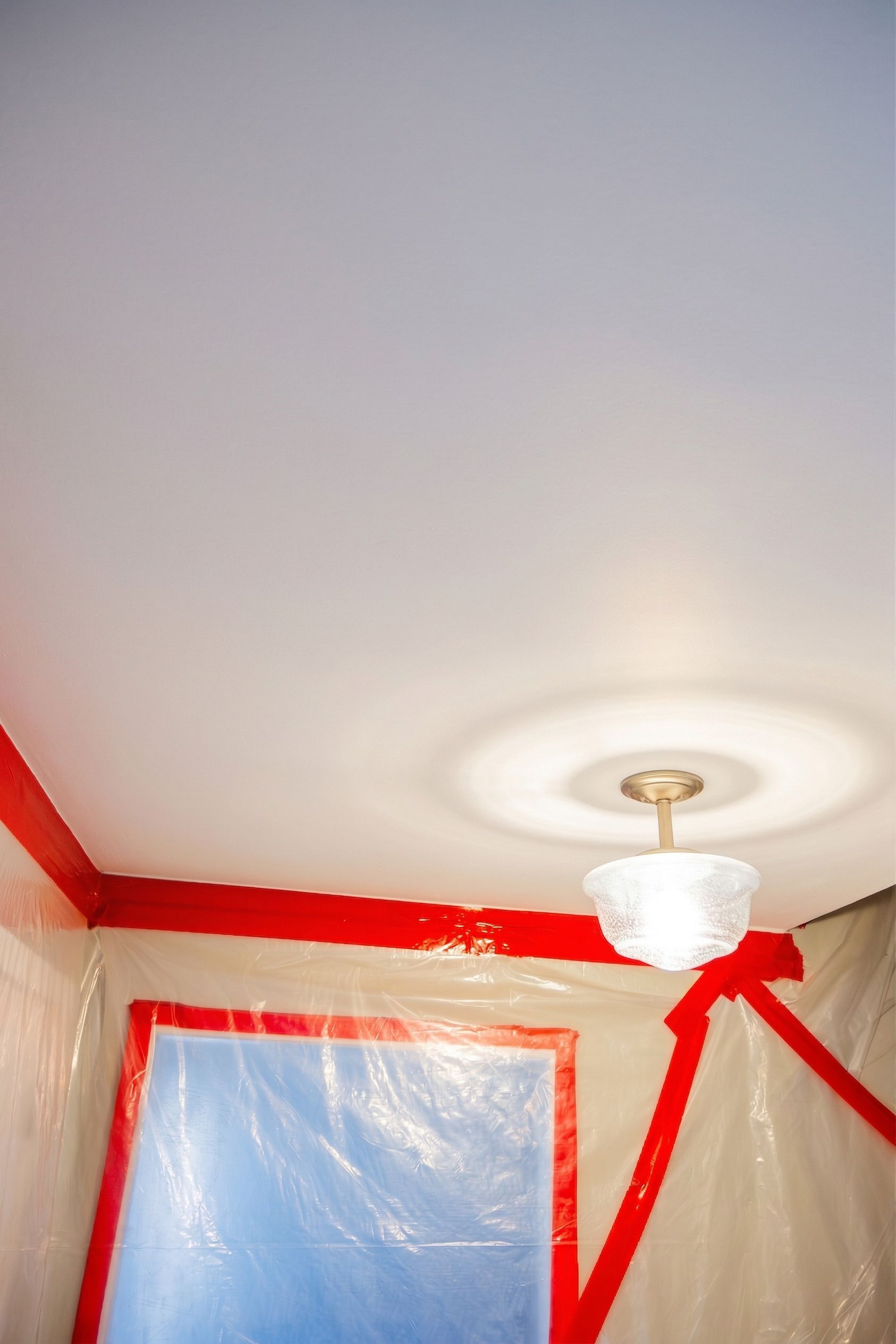 Ceiling with white light fixture, red trim, and plastic-covered walls in a room under renovation