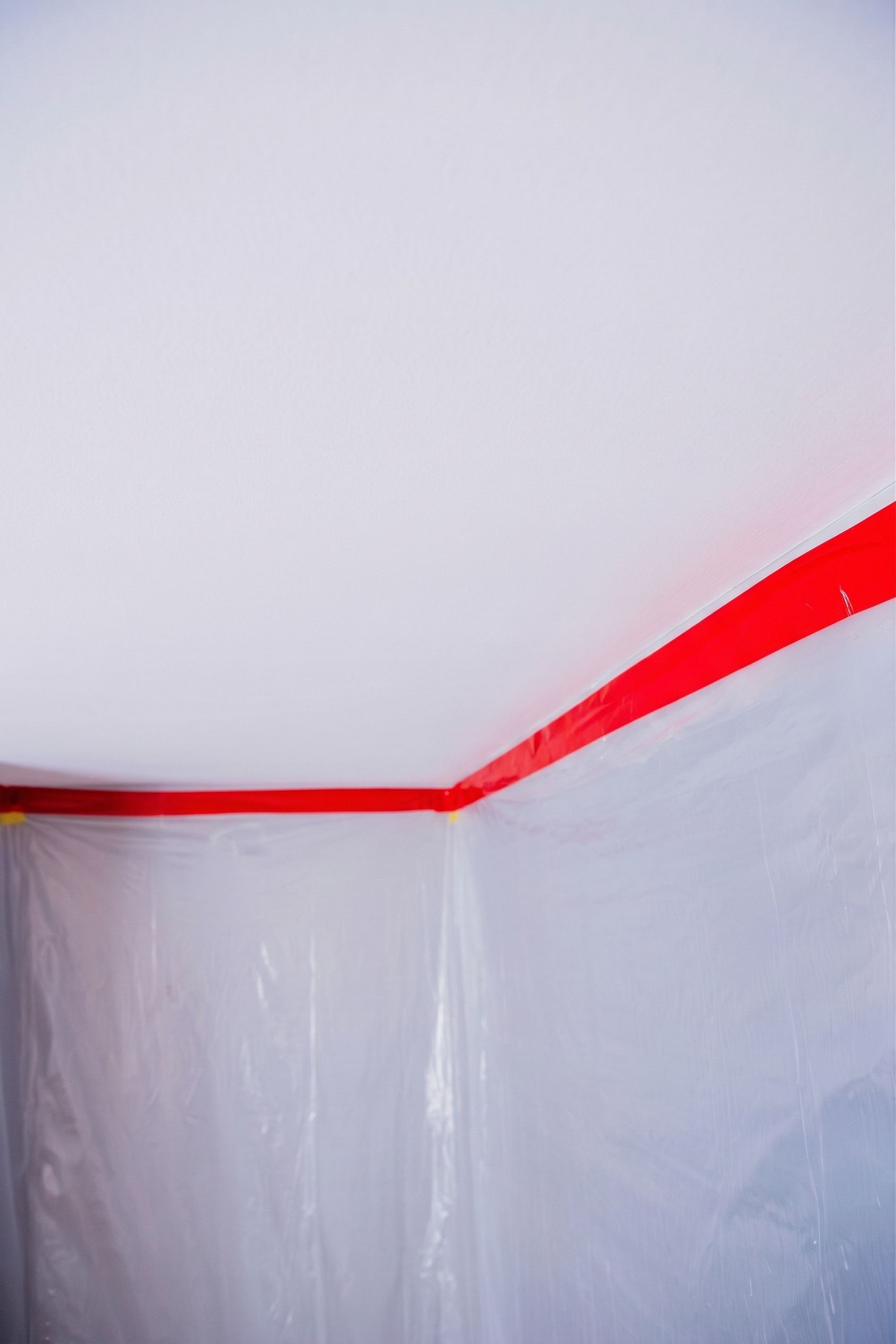 Plastic sheeting taped along a white ceiling corner, with red tape across the top edge