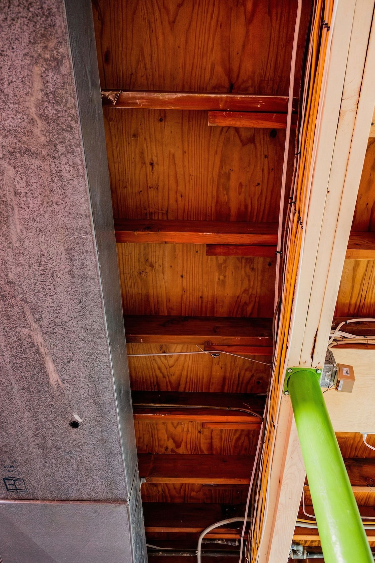Wooden ceiling beams with a bright green support pole and a gray wall edge