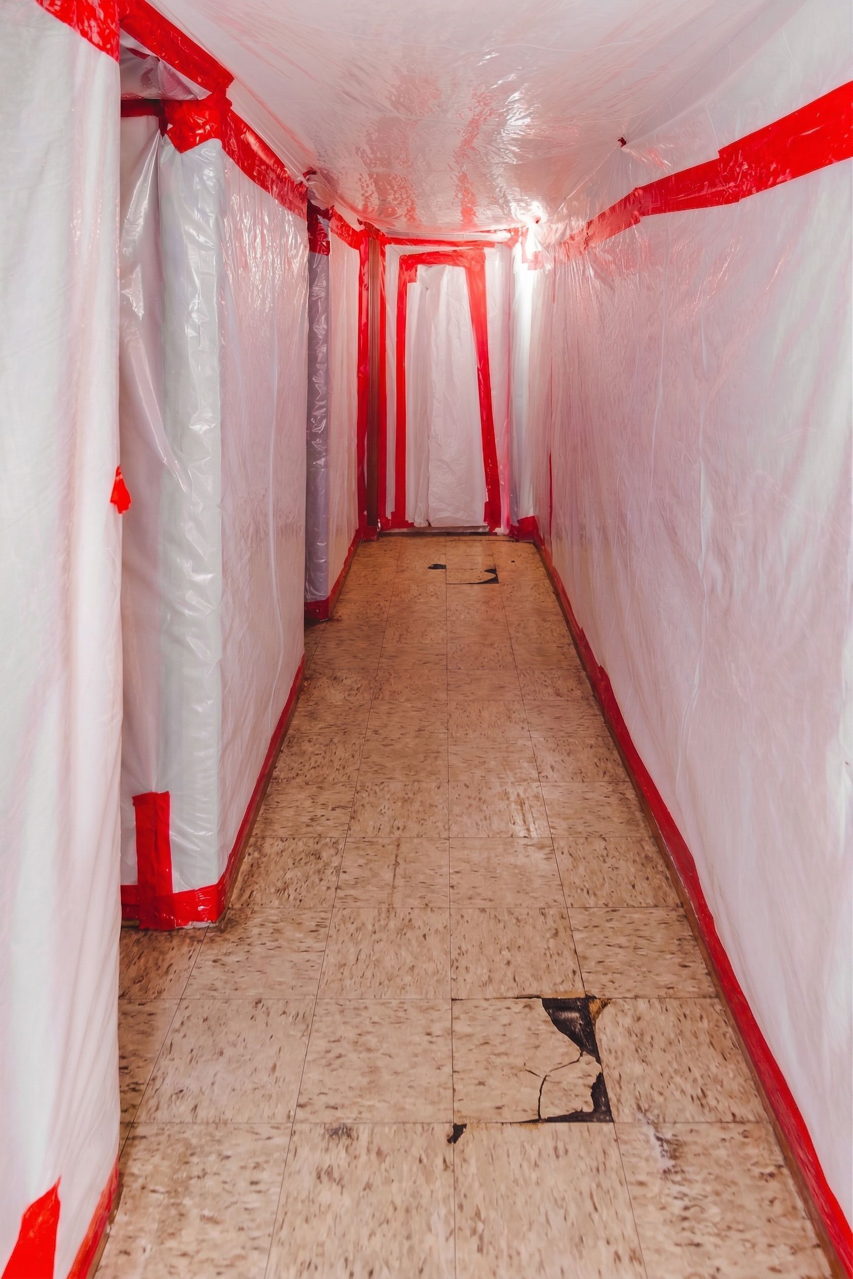 Narrow hallway covered in white plastic sheeting with red tape and a wooden floor.