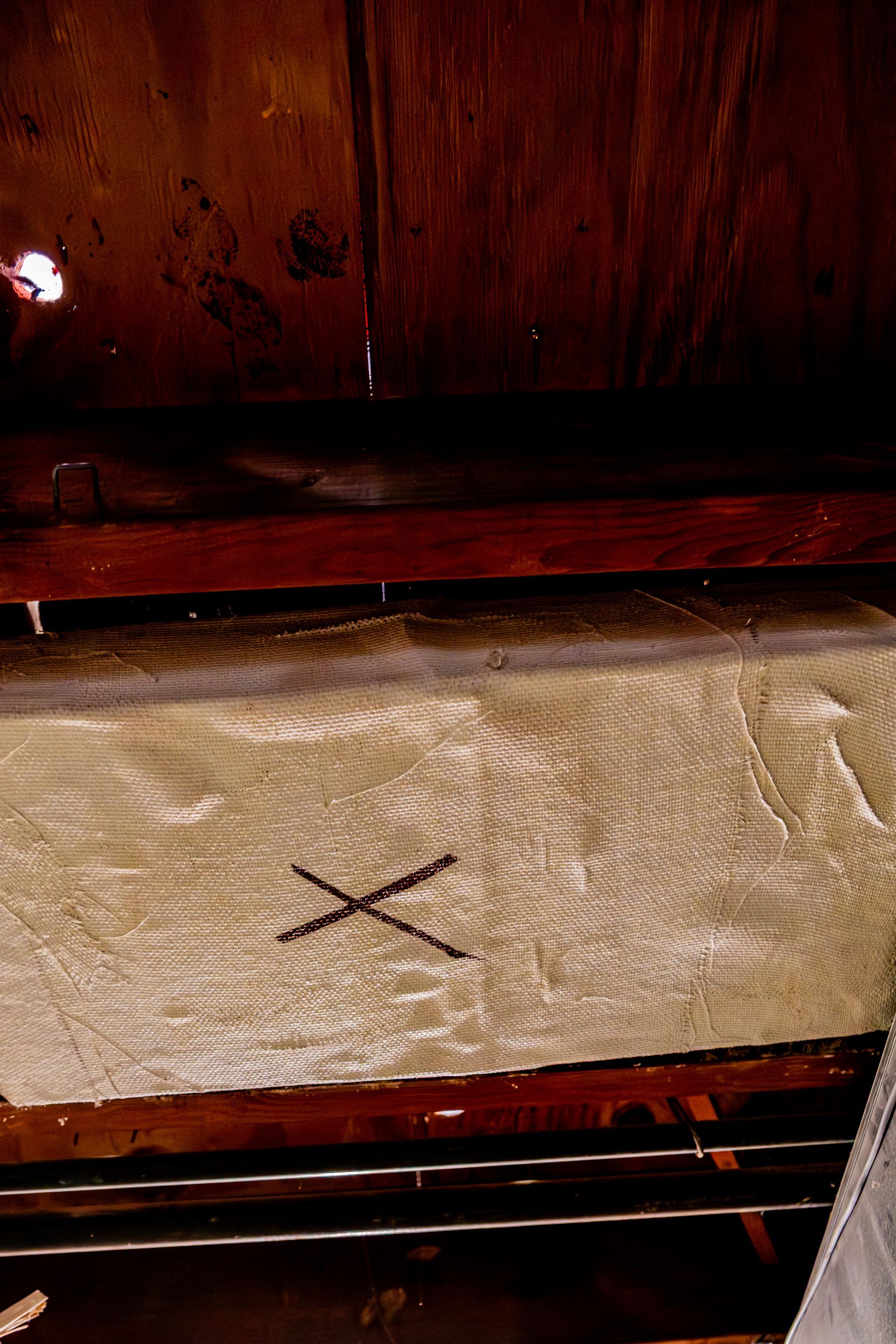 Wooden beam with a black X mark beneath a dark wood surface