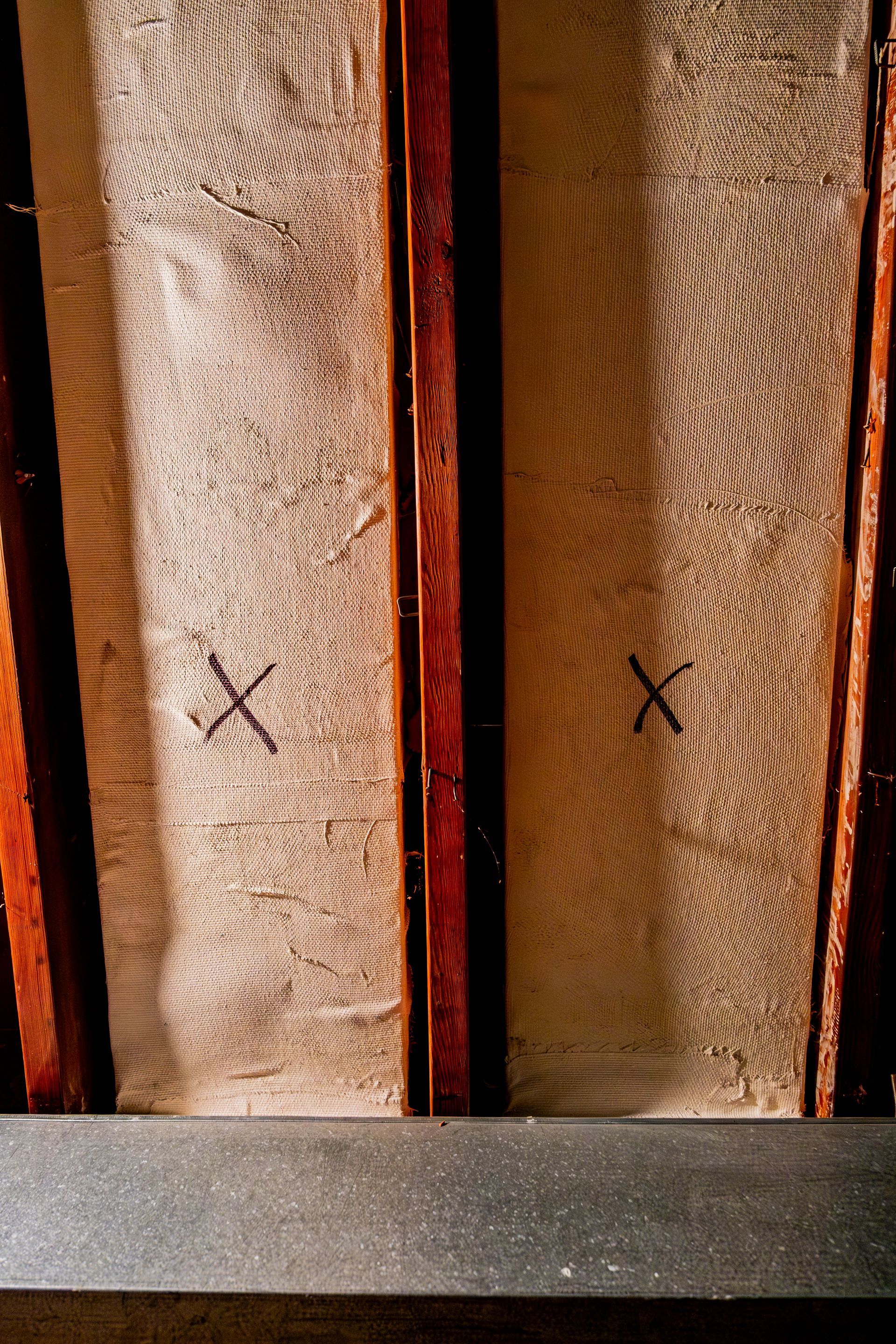 Close-up of two vertical wooden boards with black X marks beside a dark metal bar