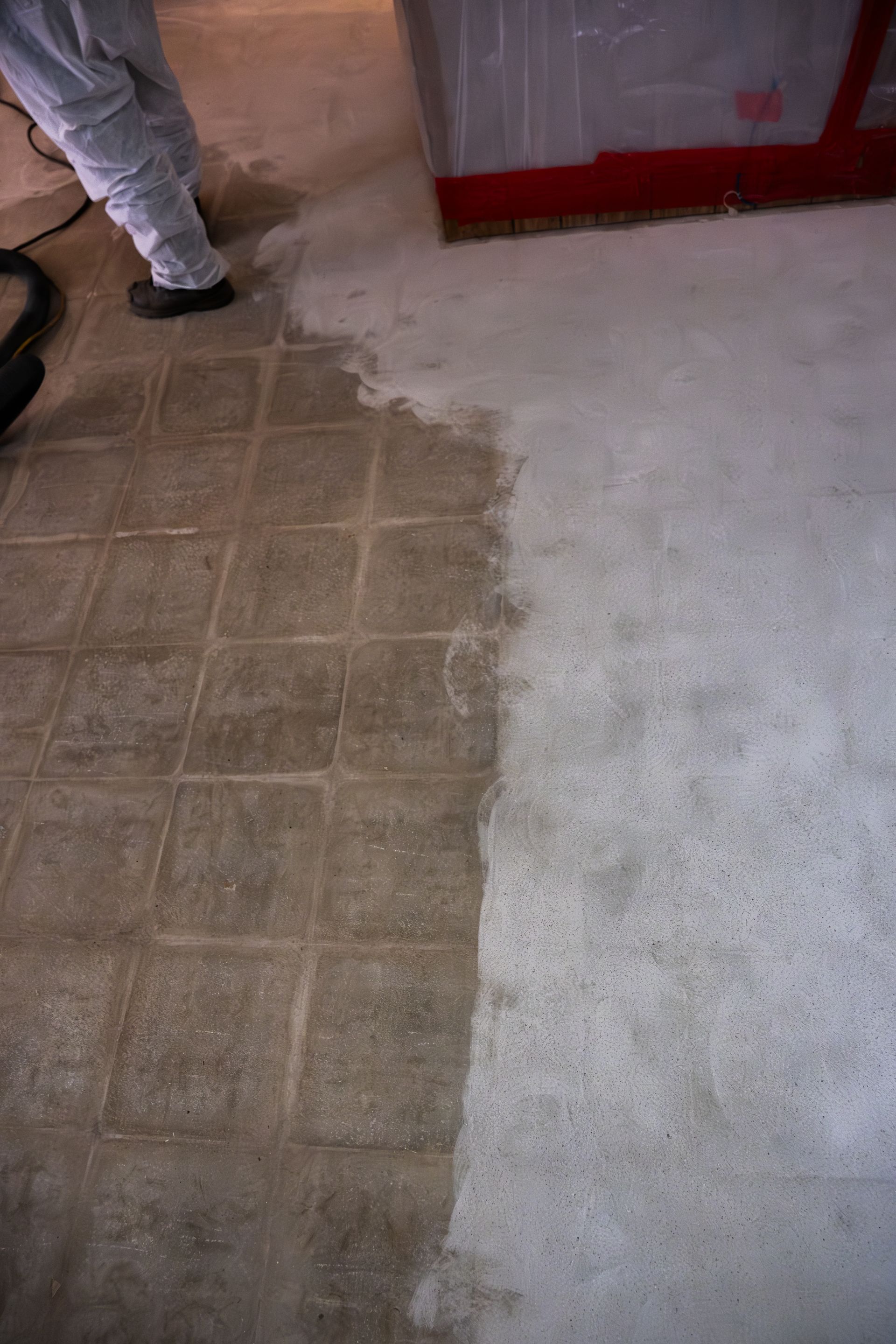 Tile floor meeting rough concrete floor, with a person’s legs visible at left.