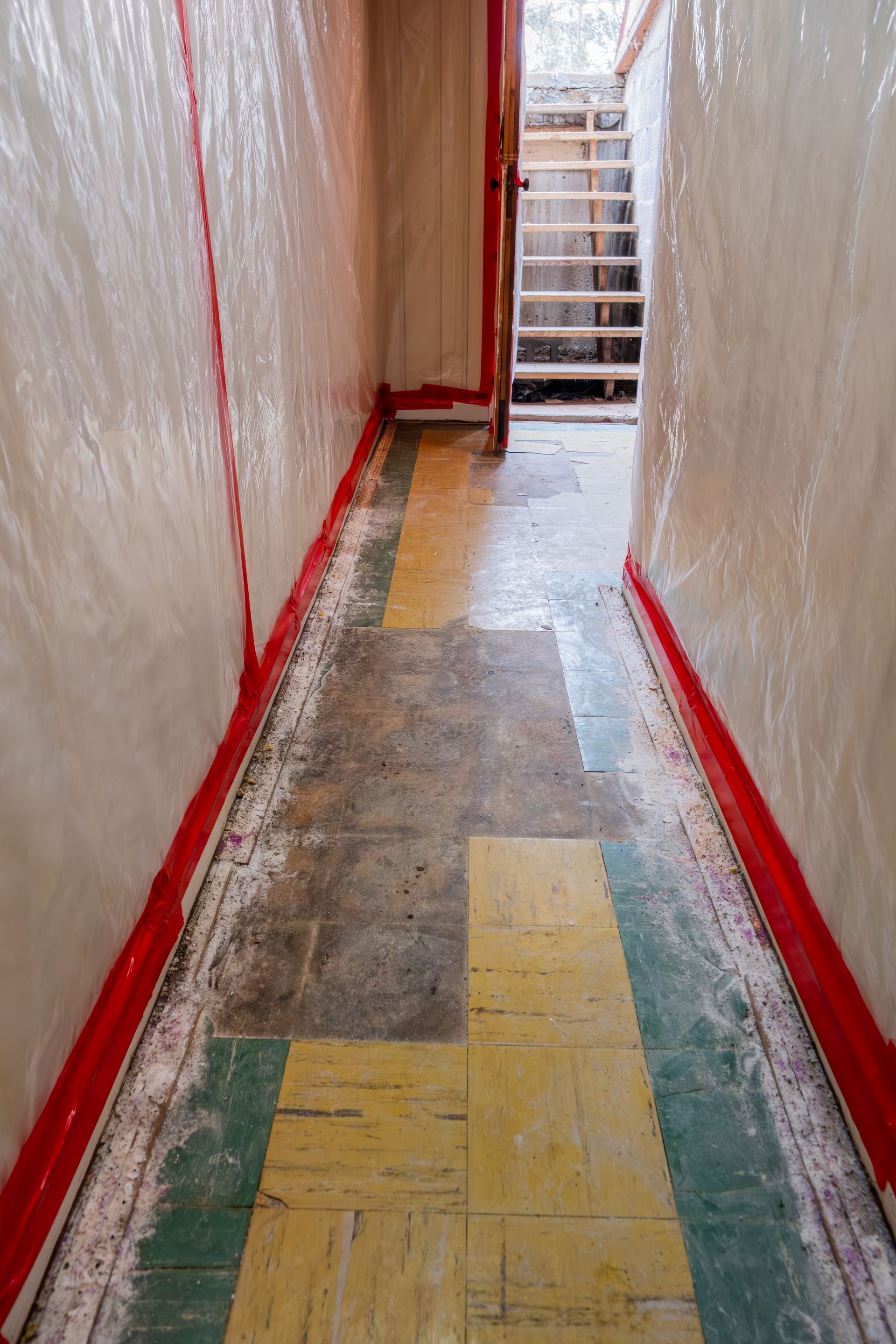 Narrow hallway under renovation with red trim, plastic-covered walls, and a ladder at the far end.