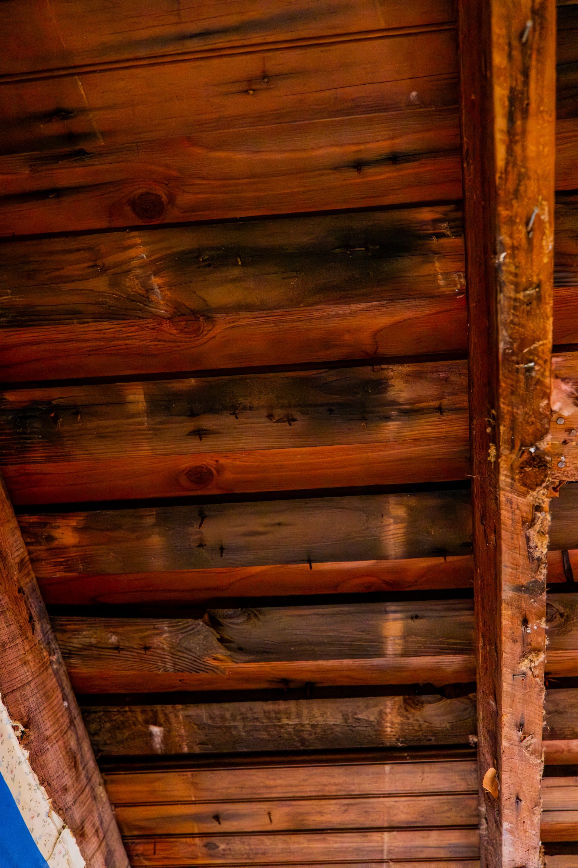 Wooden ceiling beams and planks viewed from below, with warm brown tones and dark stains