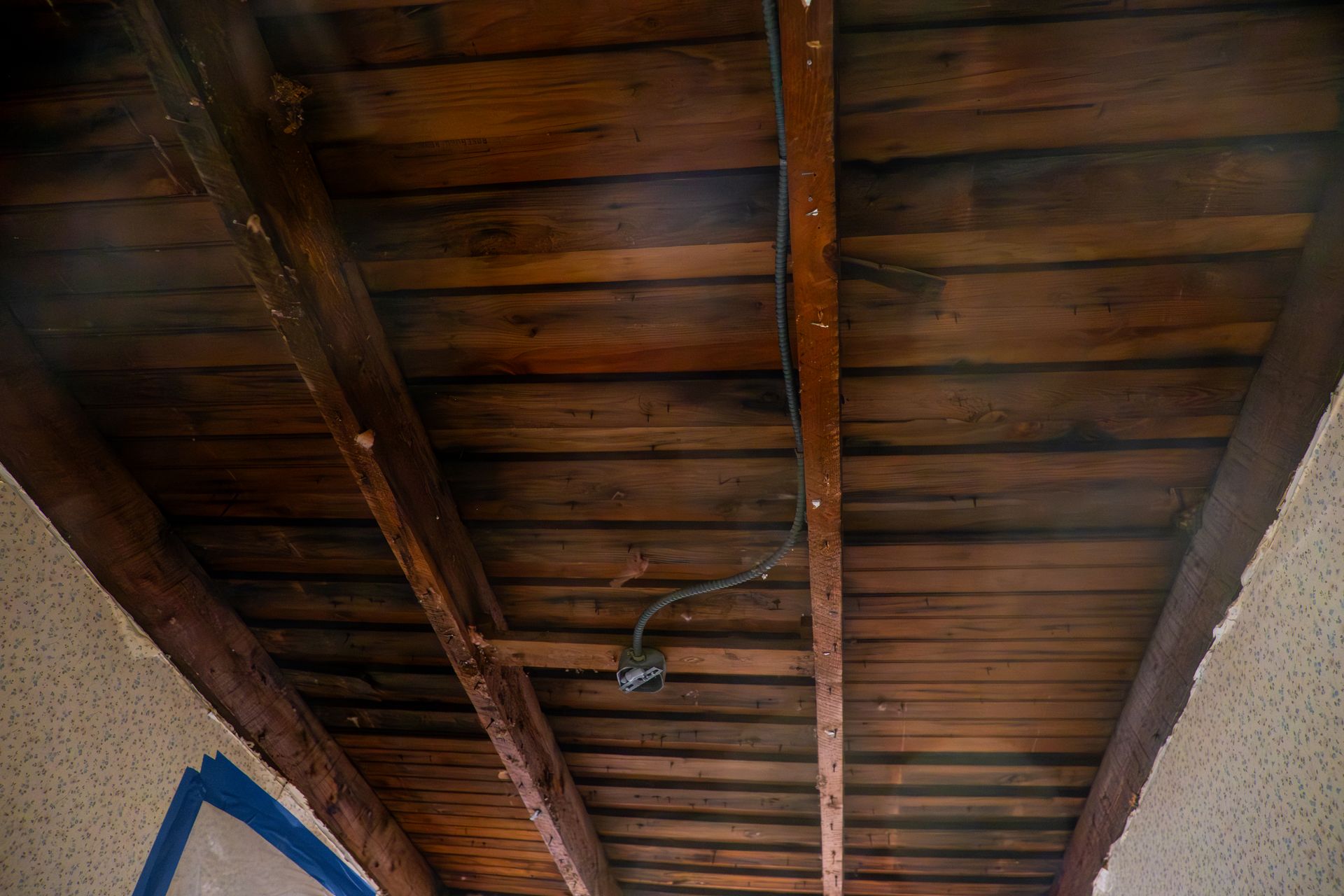 Wooden plank ceiling with exposed beams and a hanging wire in a narrow corridor