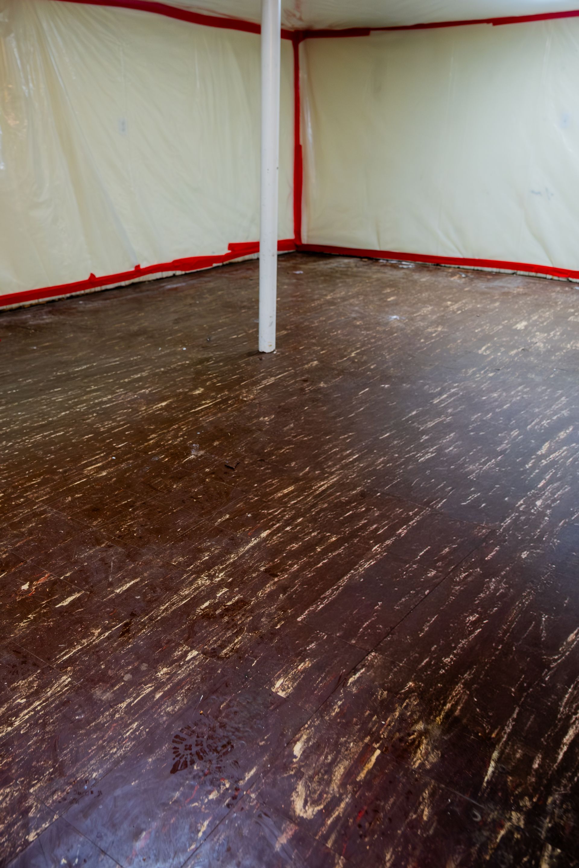 Empty tent interior with dark wooden floor, white walls, and red trim, centered around a support pole