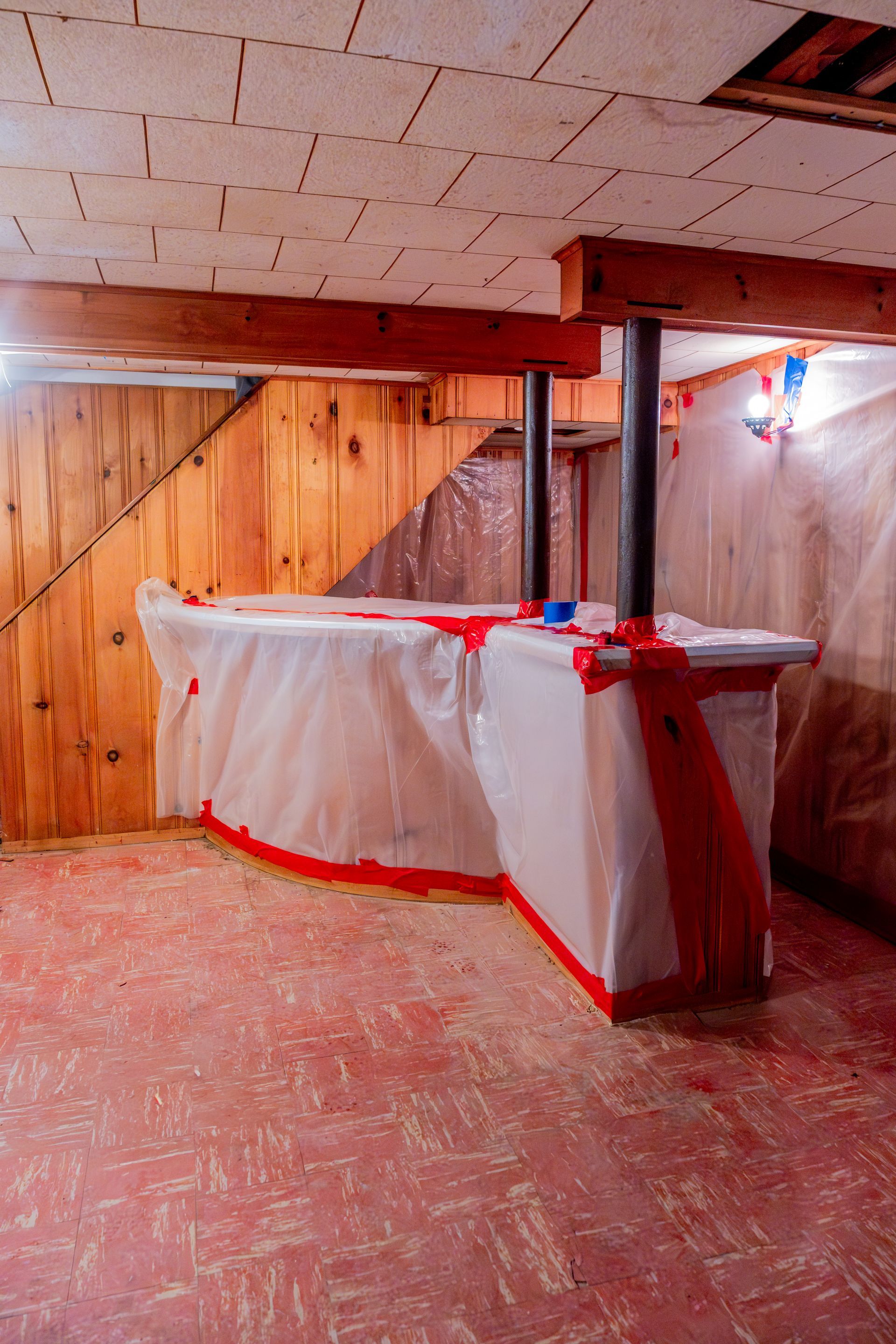 Basement room with wooden paneling, a covered table, and red tape marking areas on the floor and walls