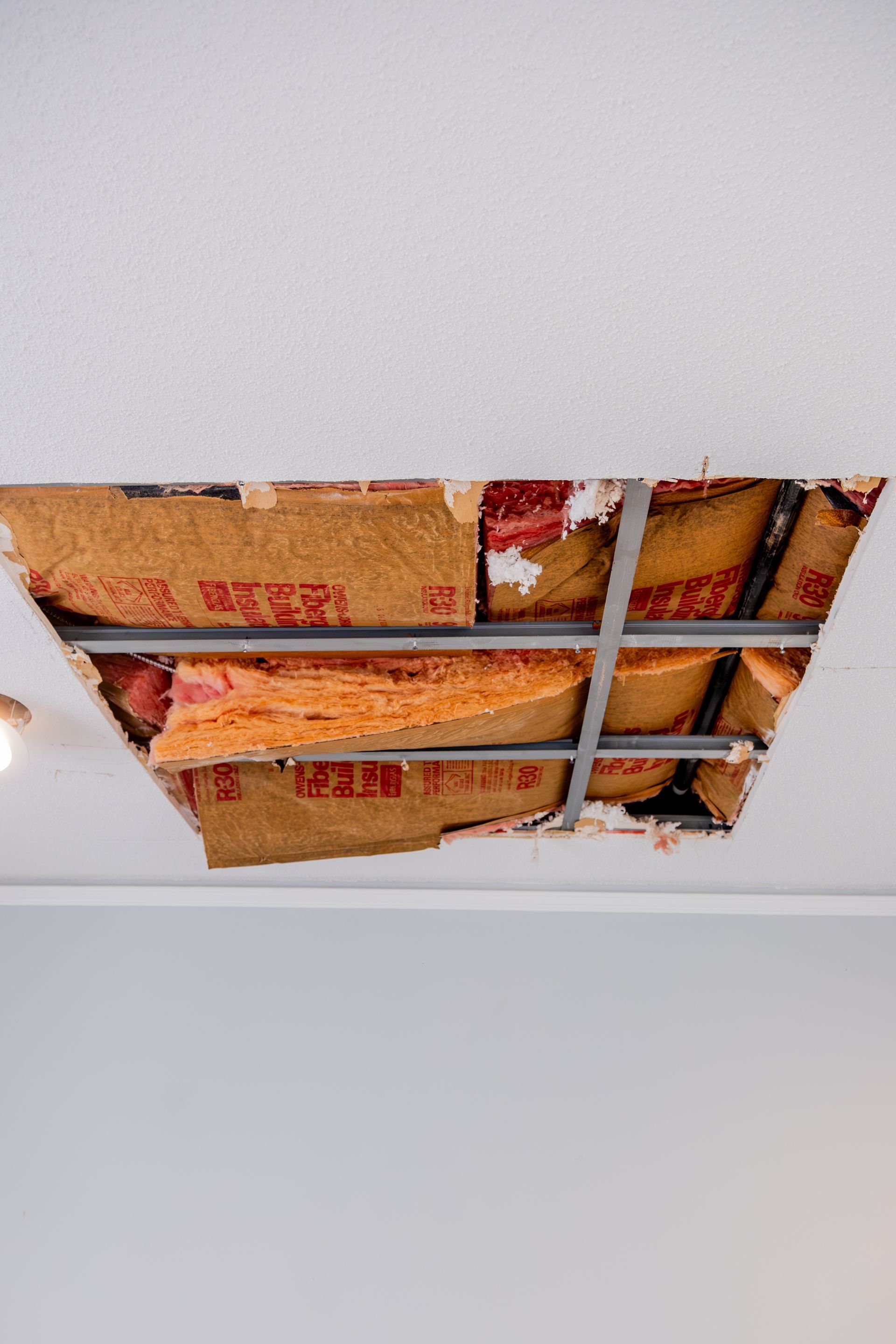 Damaged ceiling with a large hole exposing insulation and metal framing