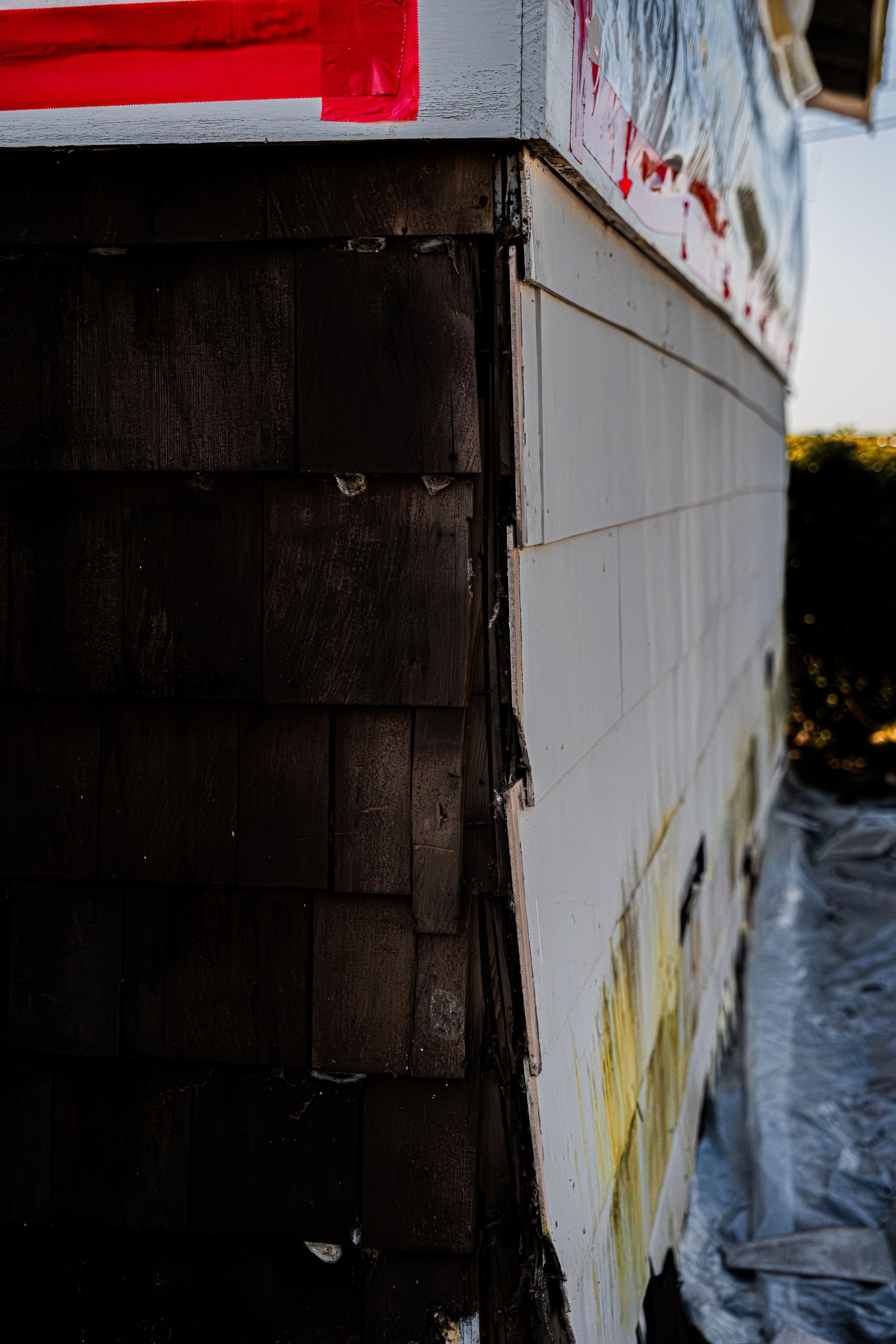 Close-up of a building corner with dark shingles, white siding, and red trim above a snowy ground