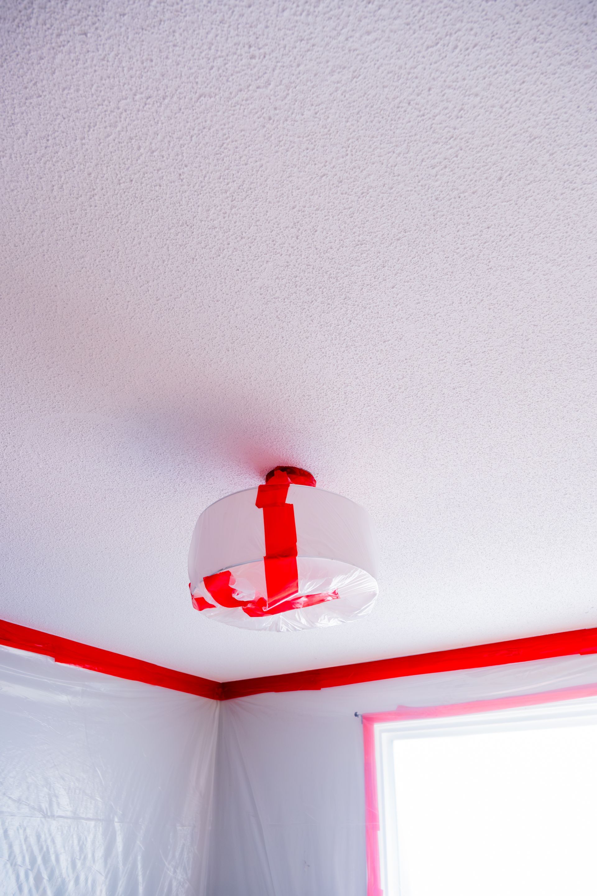 Ceiling smoke detector covered with red tape in a room with red trim and a window