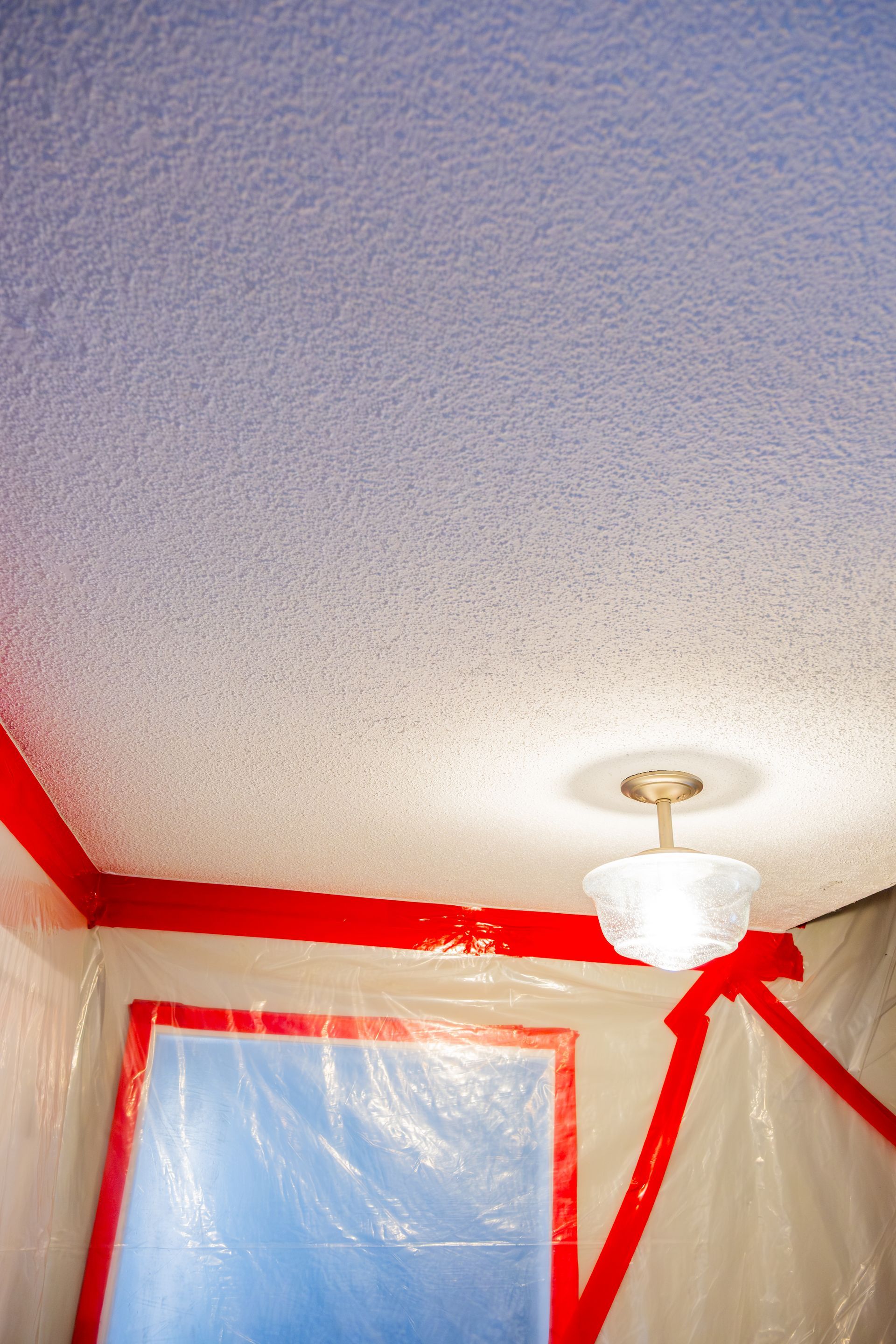 Ceiling corner with red trim, blue window covering, and a hanging light fixture in a room under renovation