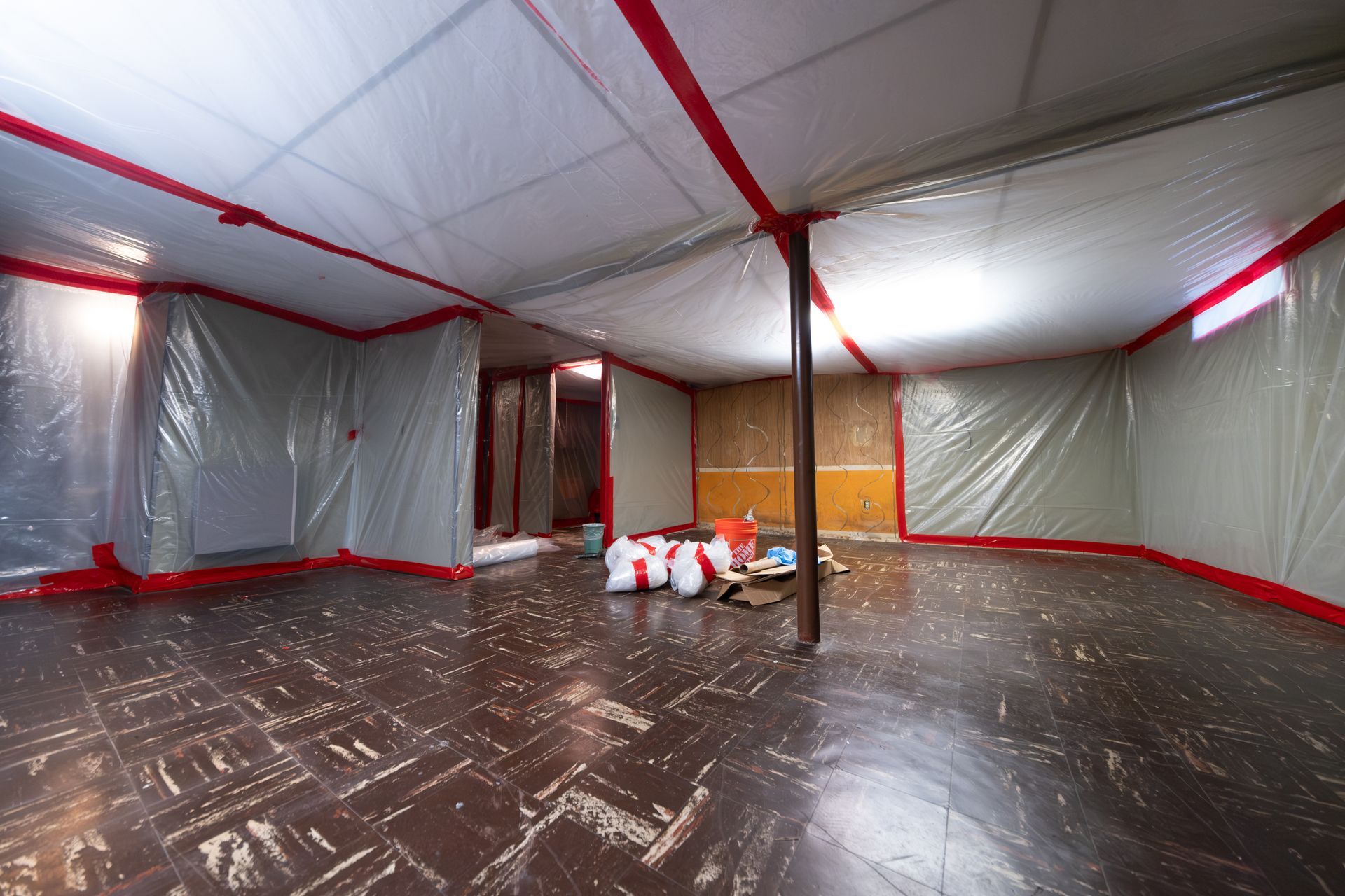 Covered room with plastic sheeting, red tape, and supplies piled near the center.