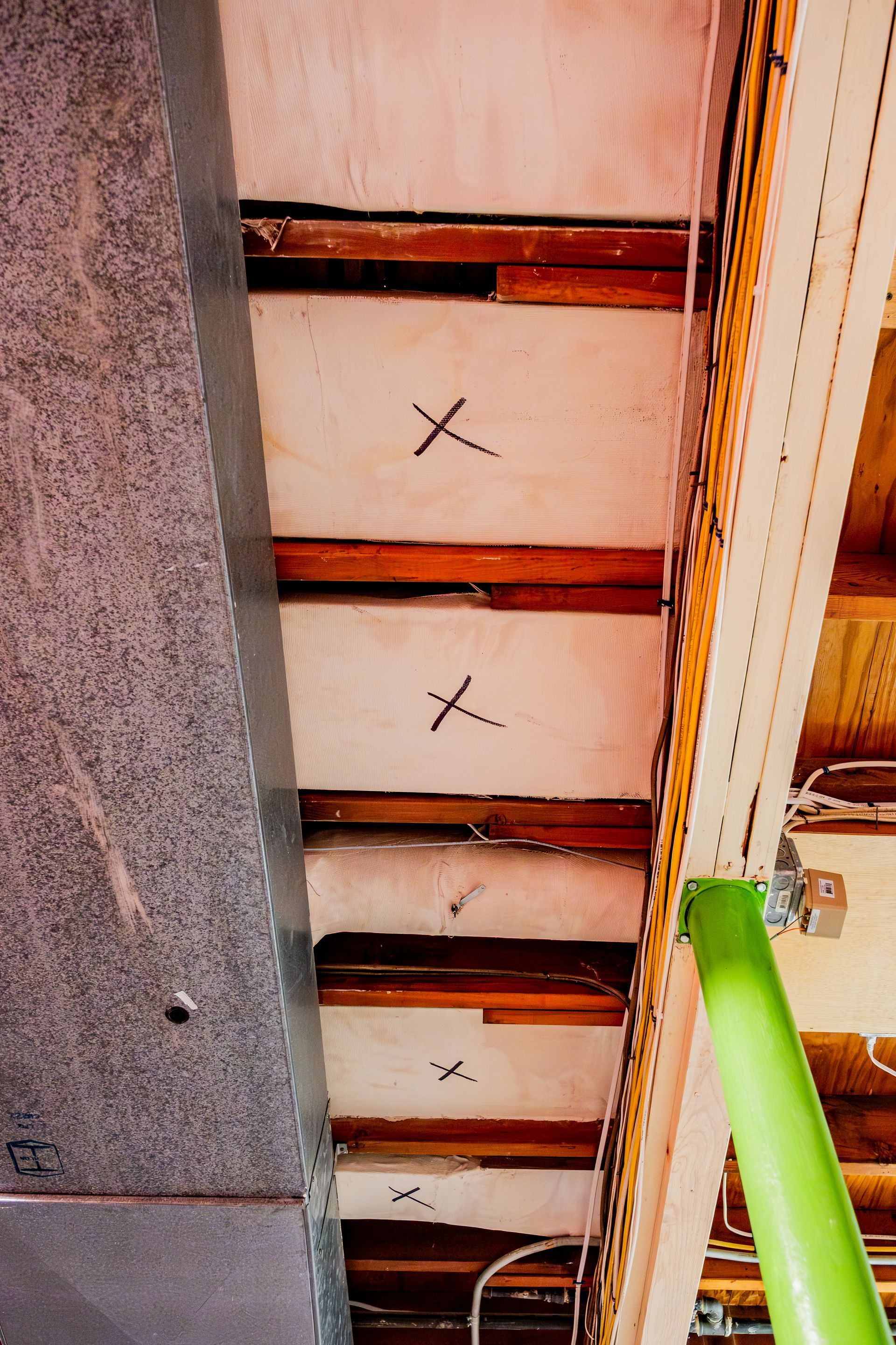 Upward view of a ceiling with exposed wooden beams, plaster panels, and a green ladder on the right.
