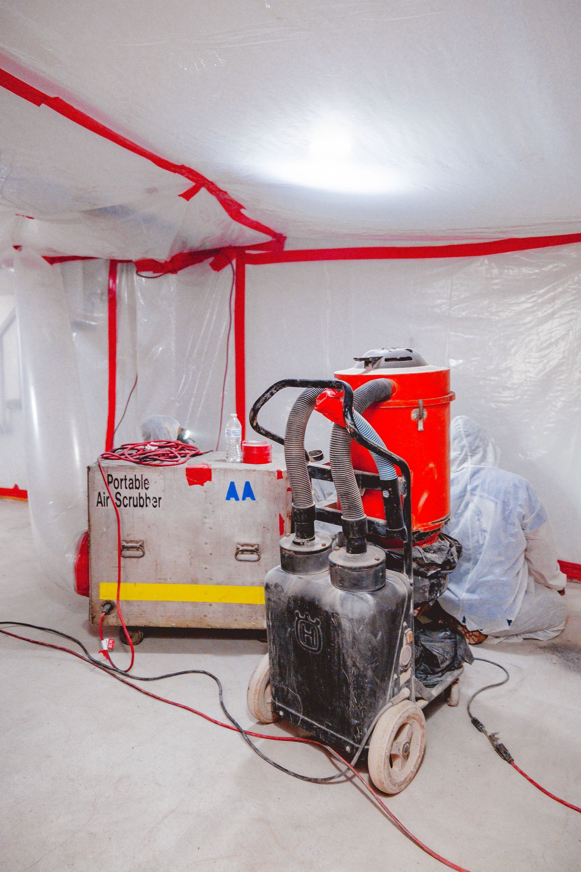 Equipment in a red-taped containment area. A machine with hoses and a red tank is next to a labeled box.