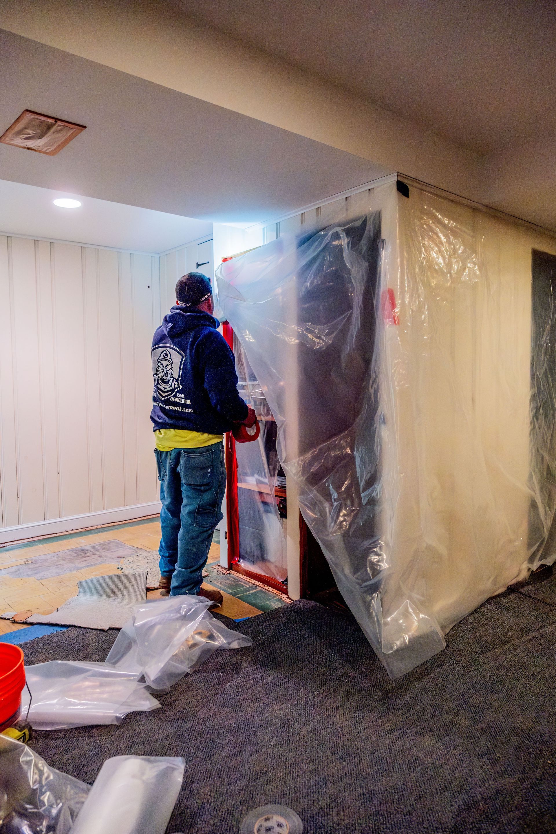 Person wrapping a large appliance in plastic in a room with flooring tools and materials