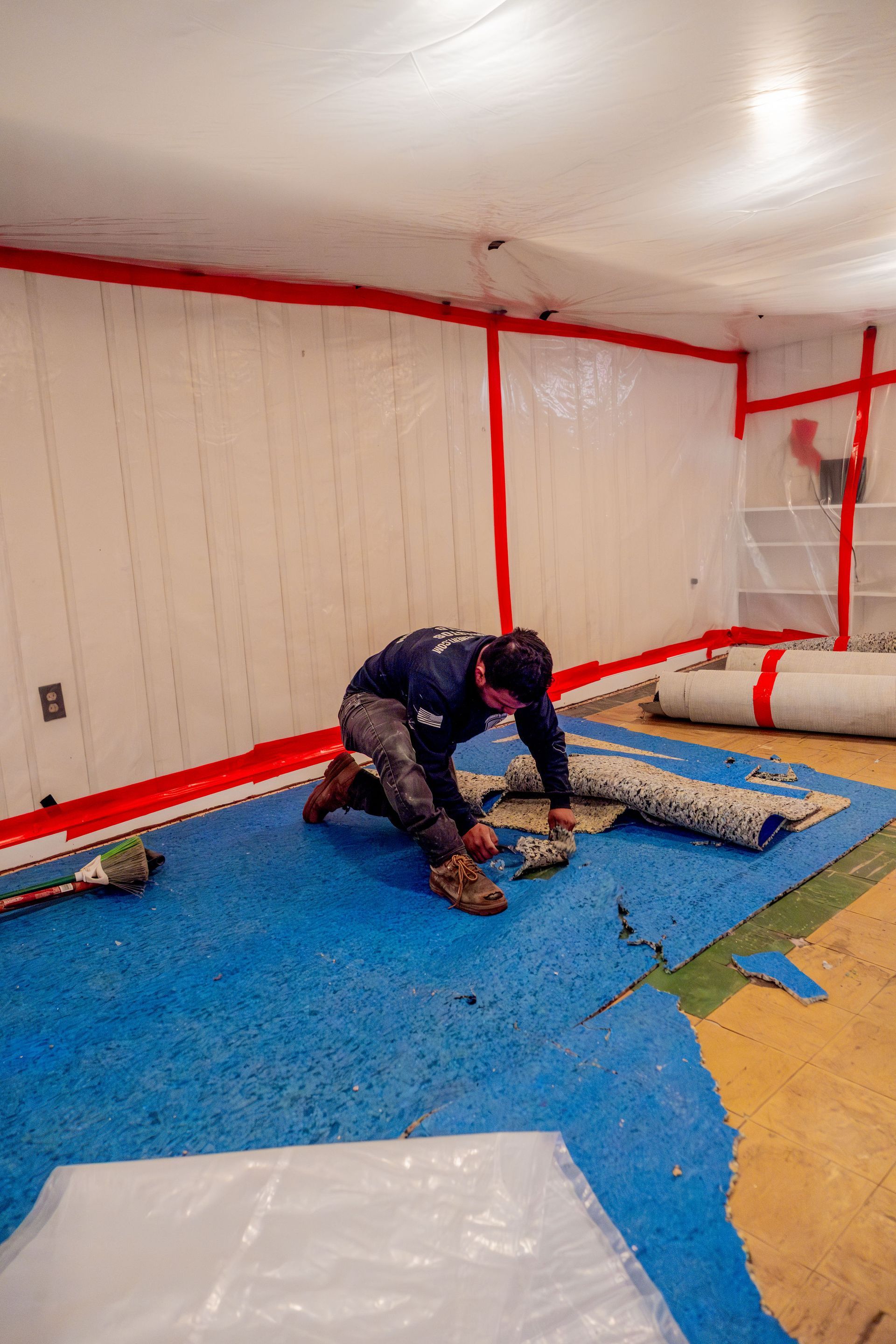 Worker kneeling on blue floor covering, installing material inside a red-bordered tented room