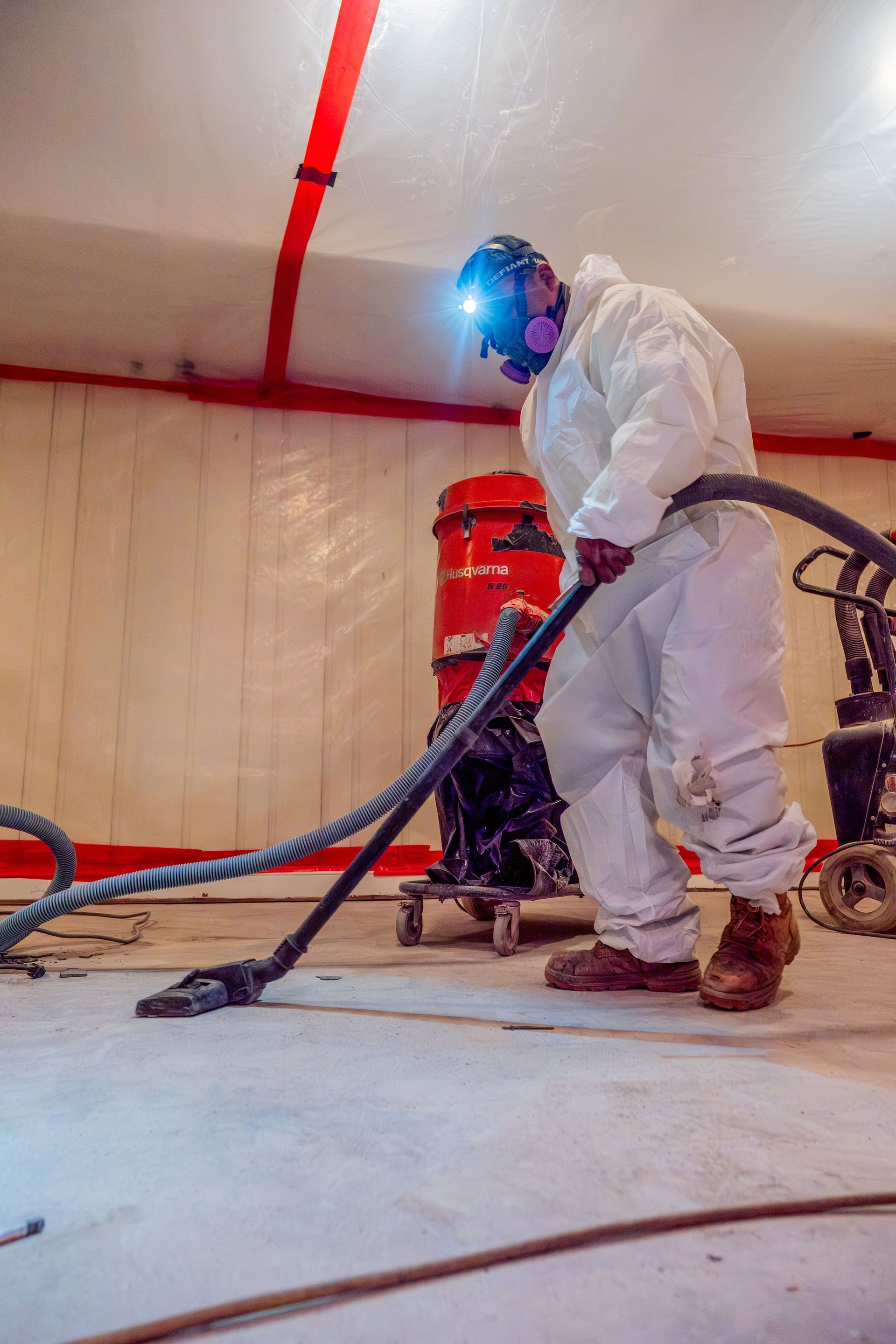 Worker in white protective suit vacuuming dust in a room with a red industrial machine
