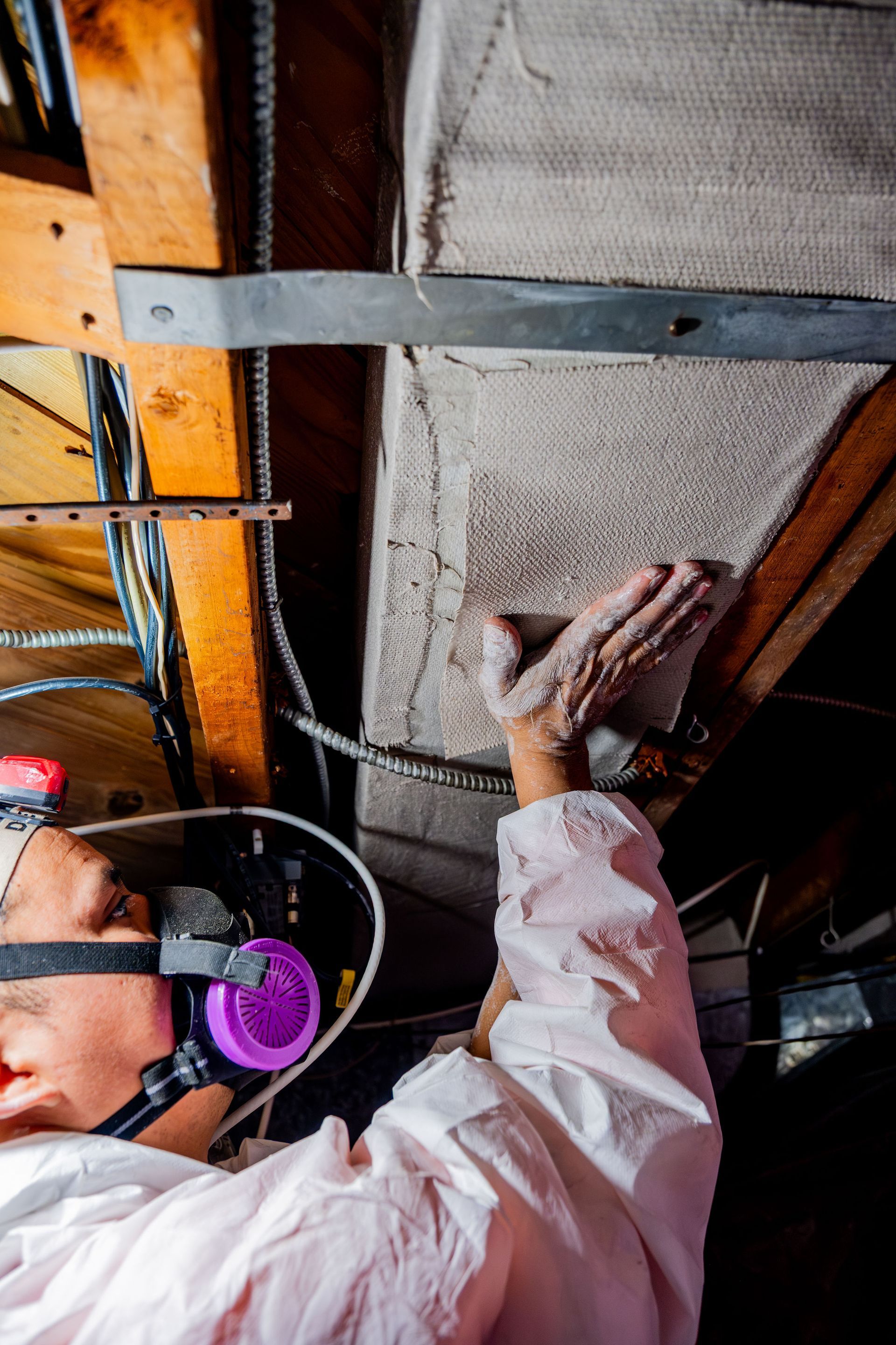 Worker installing insulation on a ceiling, wearing a hard hat and gloves in an unfinished attic