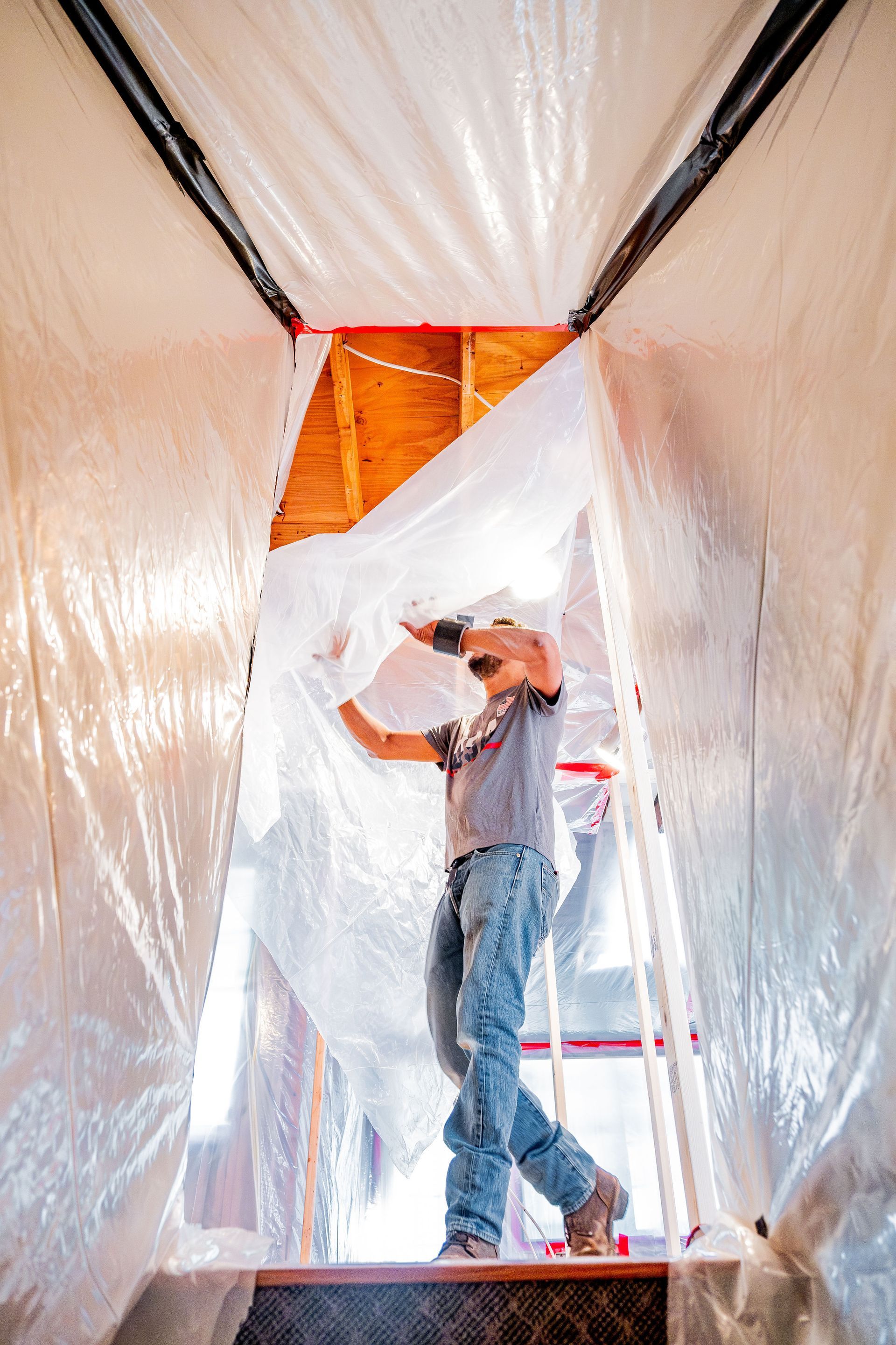 Worker installing insulation inside a plastic-covered doorway frame.