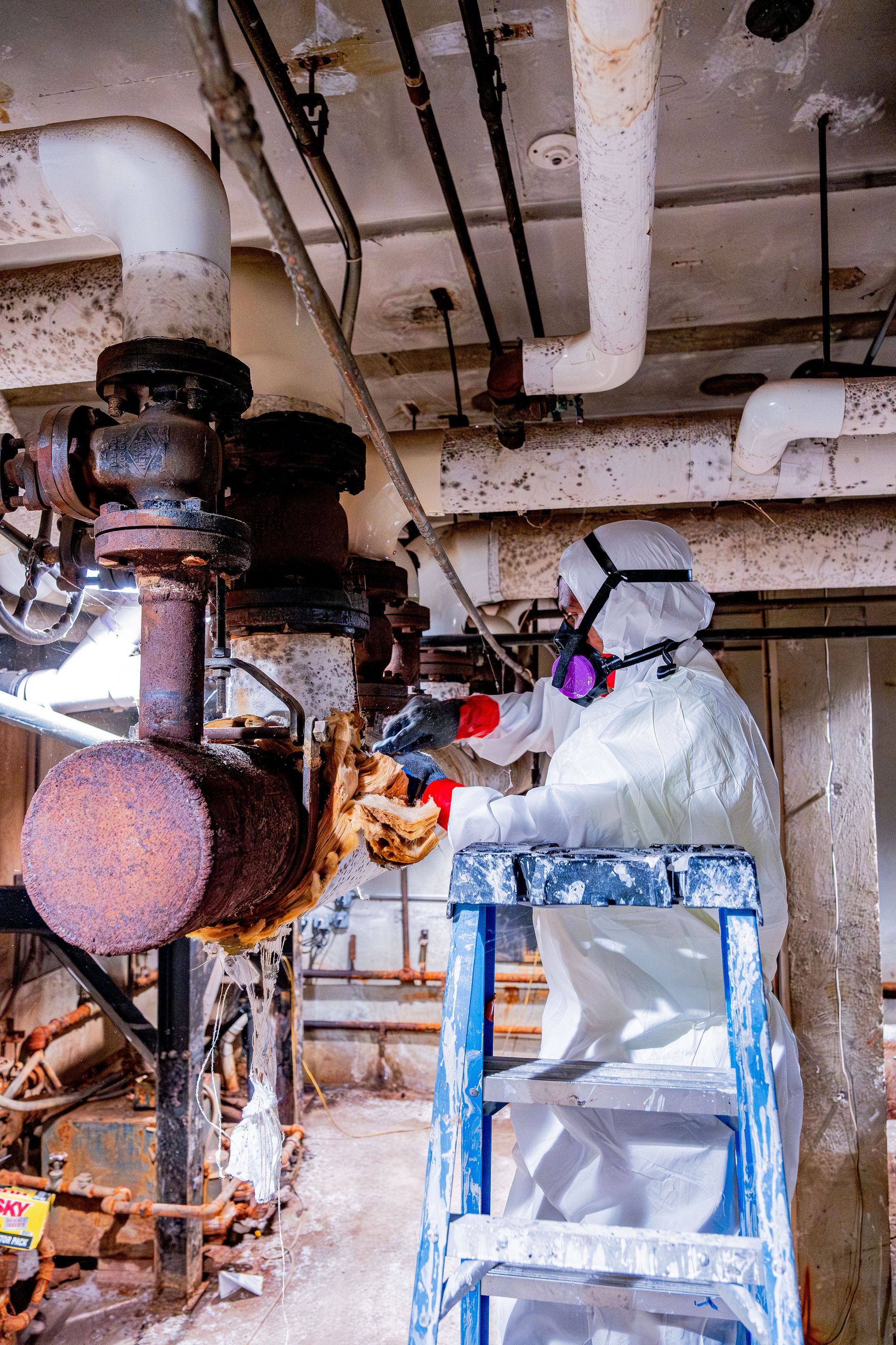 Worker in protective suit inspecting industrial piping in a factory basement