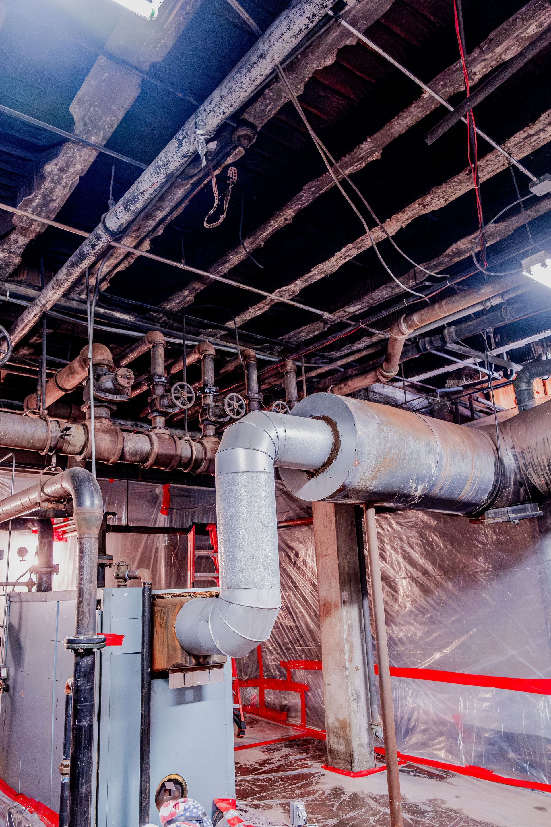 Industrial basement with exposed pipes, ductwork, and concrete walls in dim lighting.