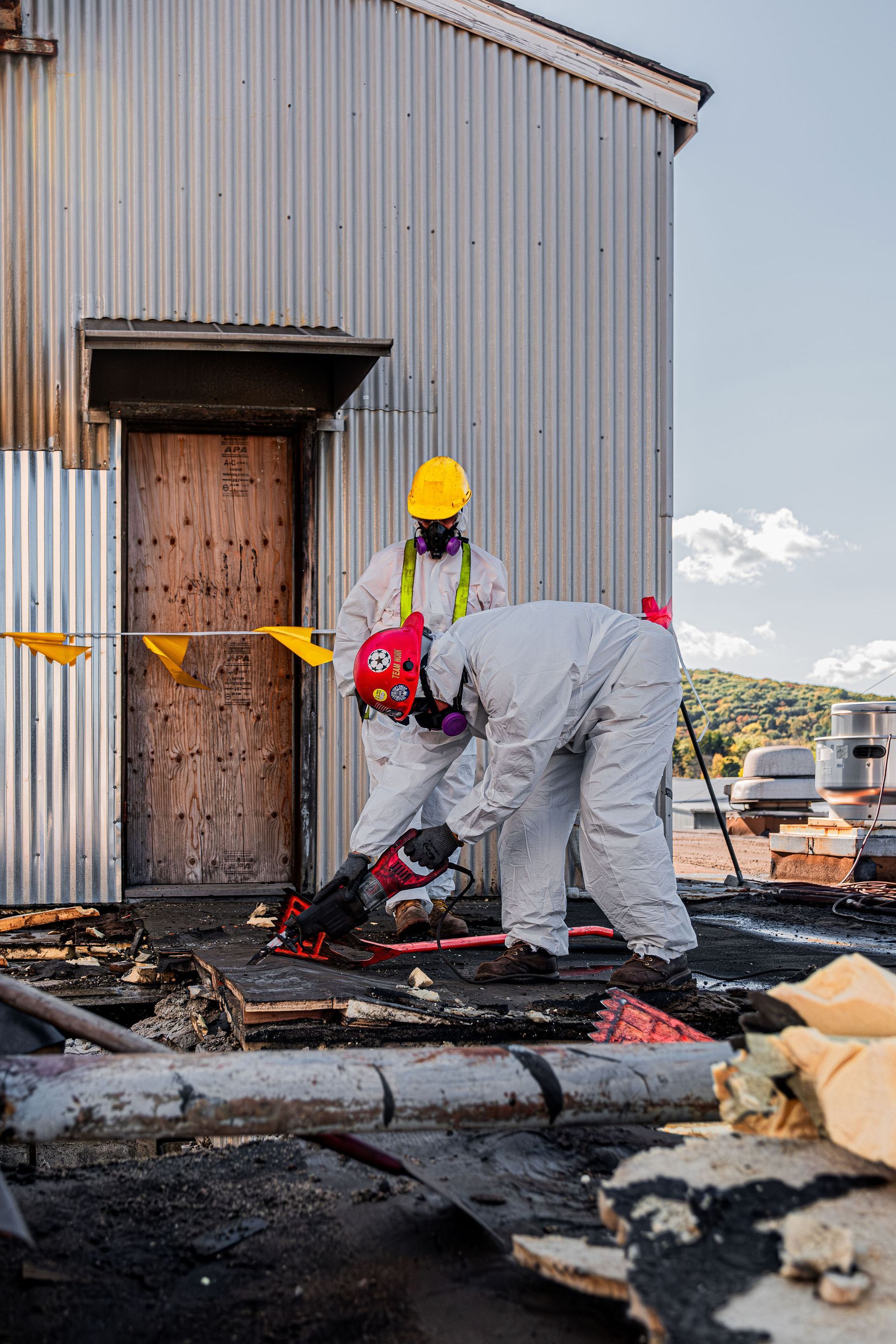 Two workers in protective gear inspect a fire-damaged building exterior.