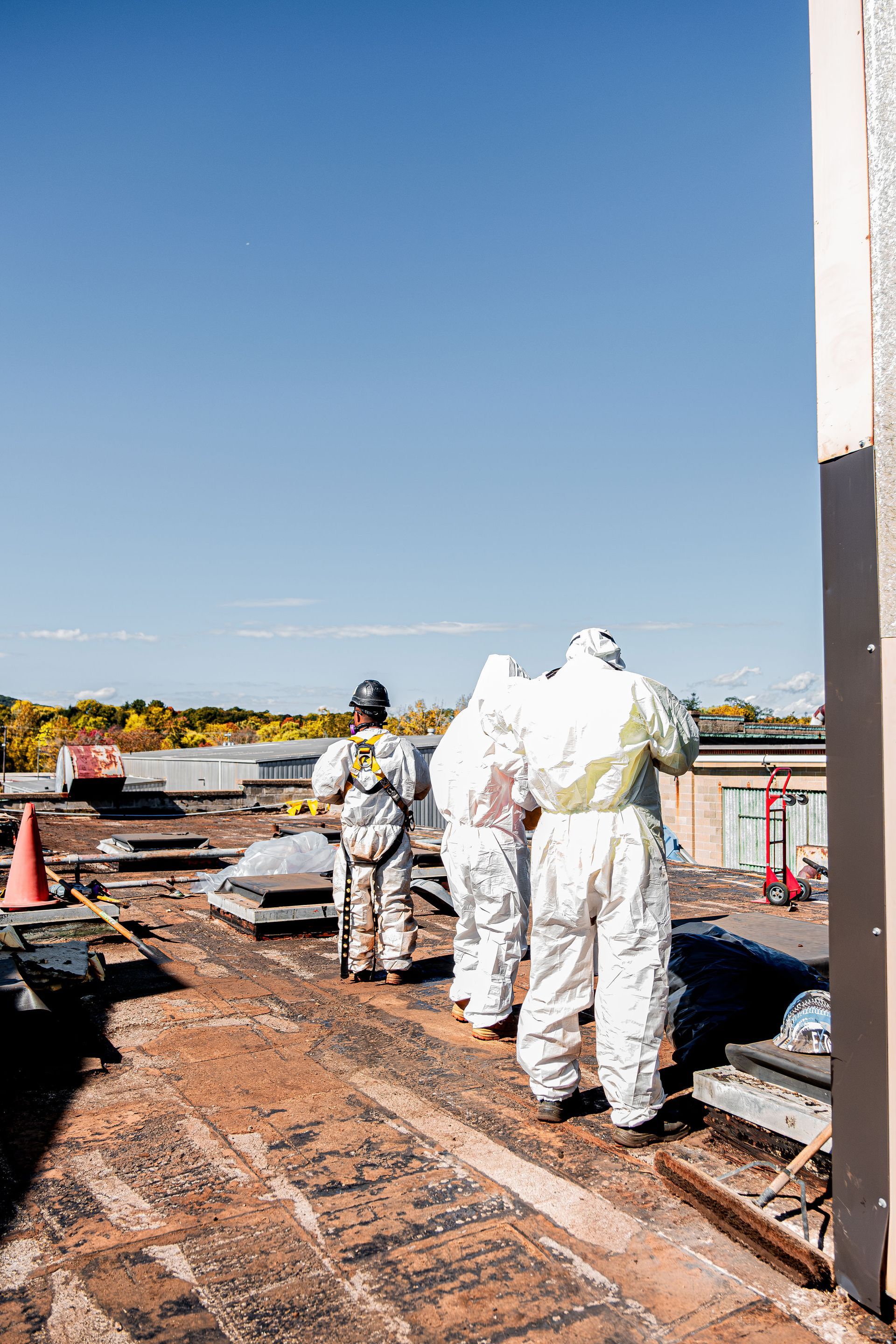 Workers in white protective suits stand on a rooftop construction site under a clear blue sky.