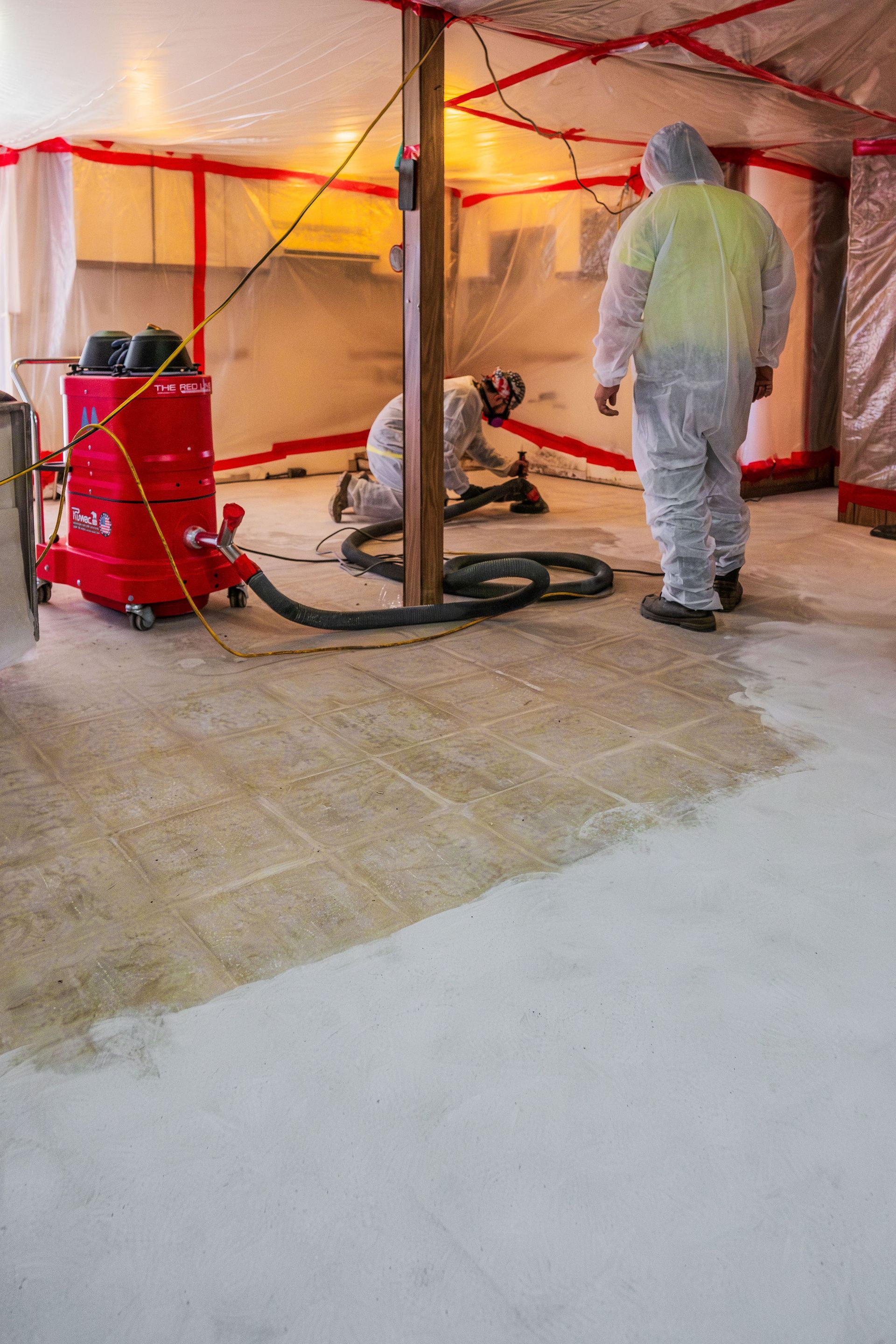 Workers in hazmat suits cleaning a flood-damaged room with industrial equipment