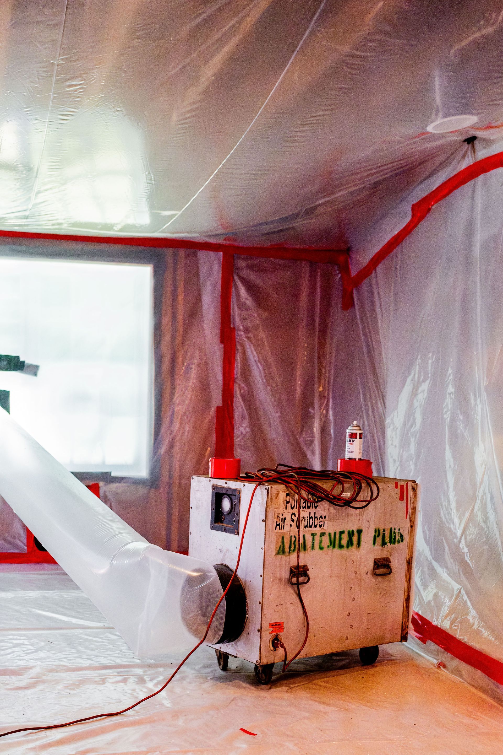 Red-painted room wrapped in plastic, with a floor blower and dust-protection setup in the corner.