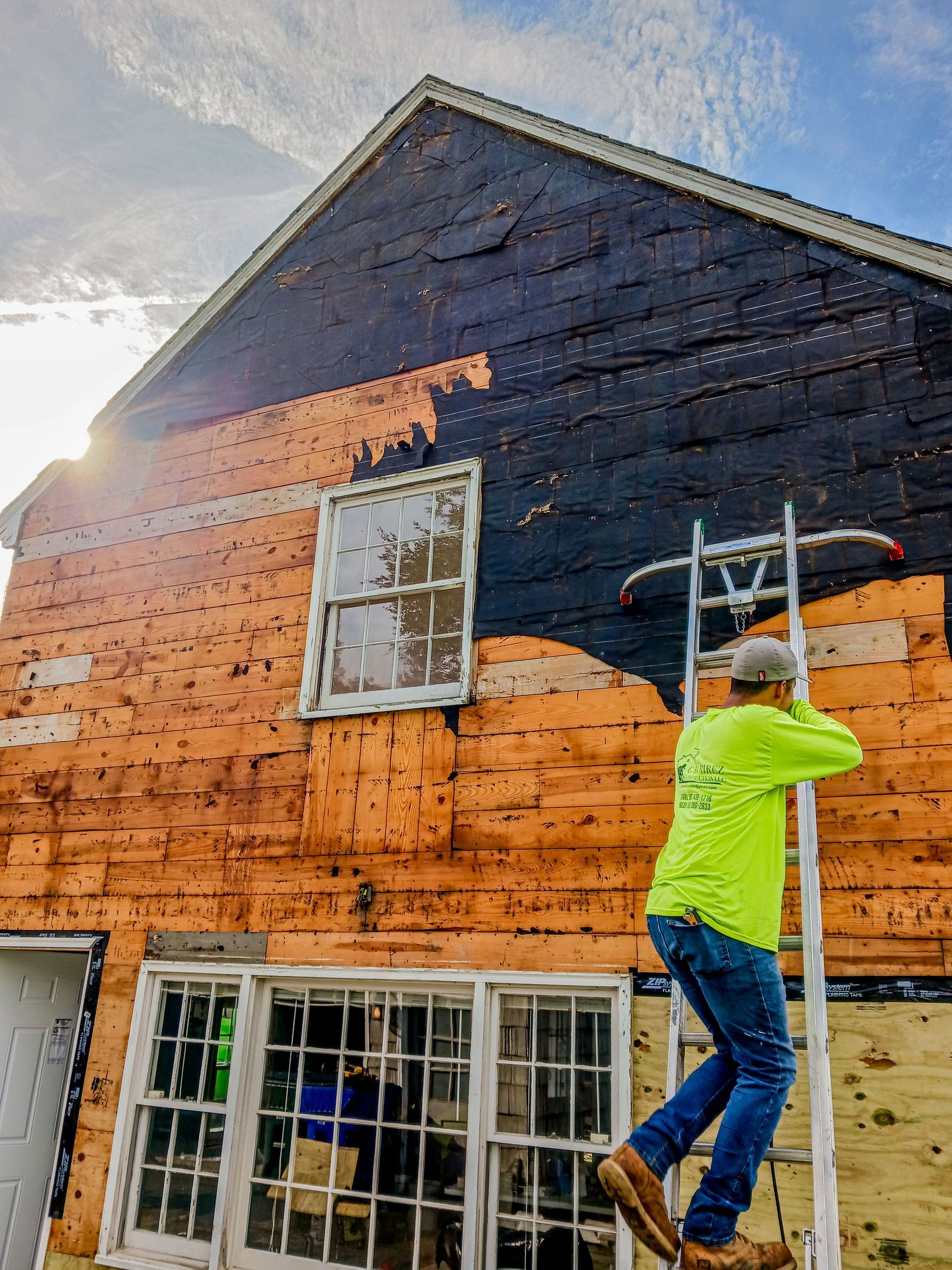 Person on a ladder painting the exterior of a house orange and dark blue under a bright sky
