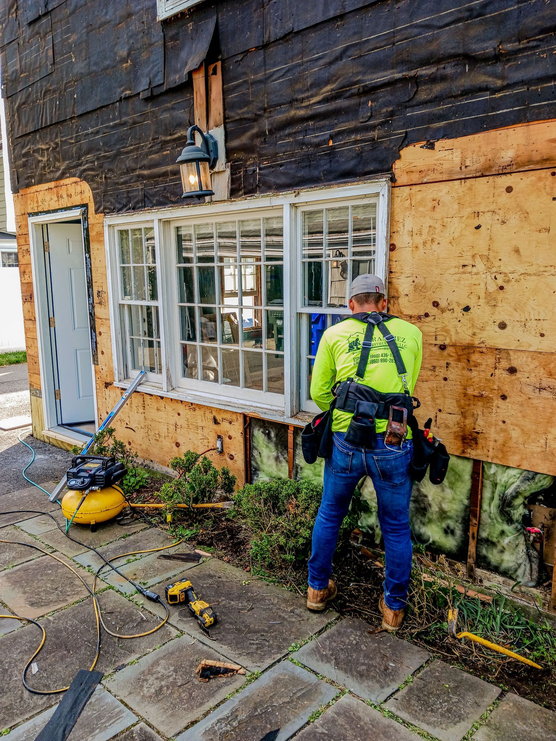 Worker in hi-vis jacket repairing a house exterior beside a window and boarded wall