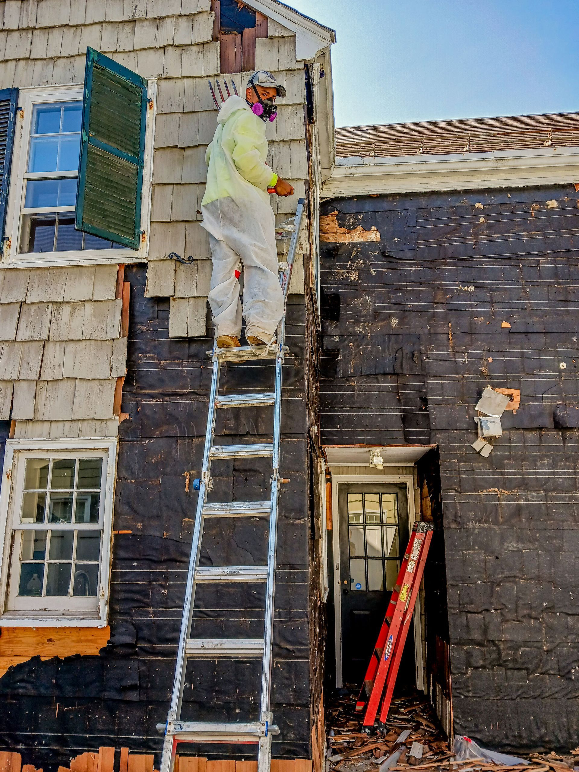 Worker in white protective suit painting a house exterior from a ladder