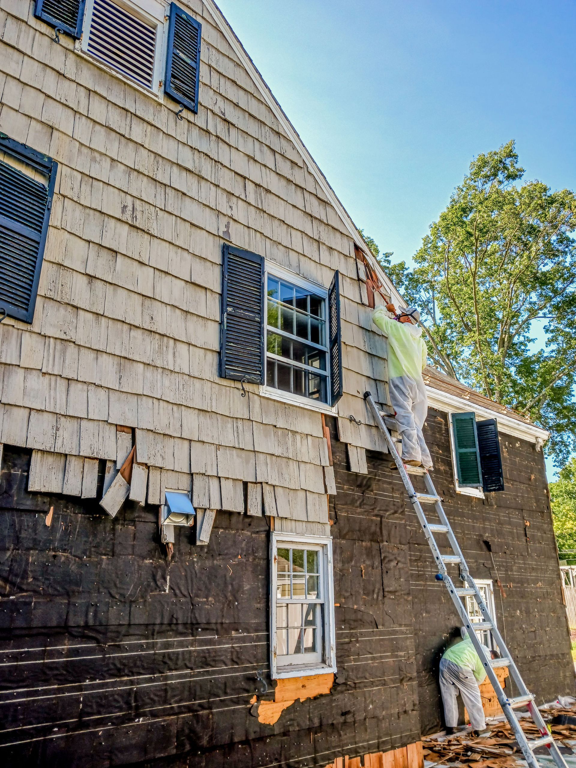 Worker on ladder repairing shingle siding on a house exterior