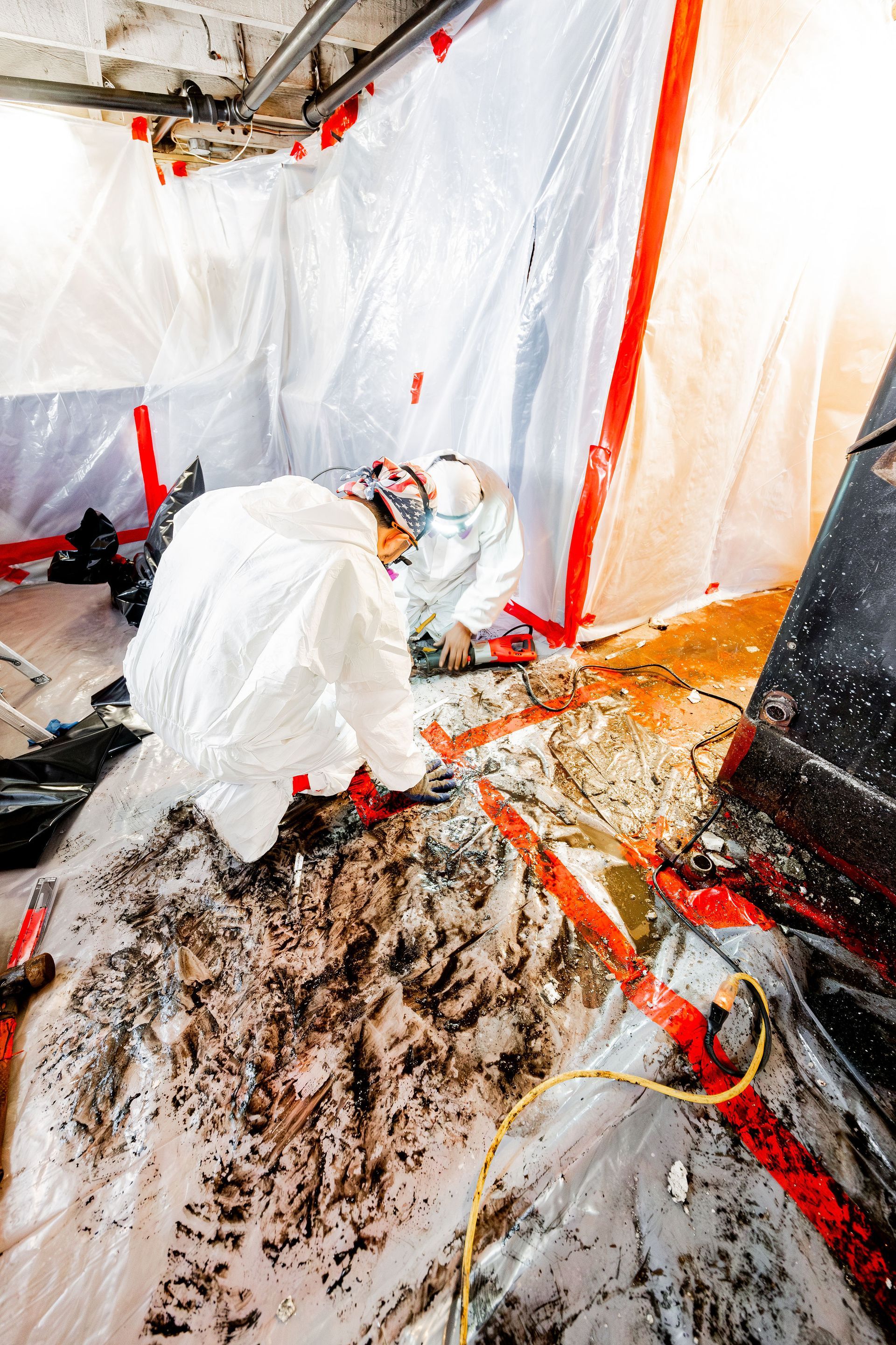 Worker in white protective suit cleaning a debris-covered floor in a plastic-covered room