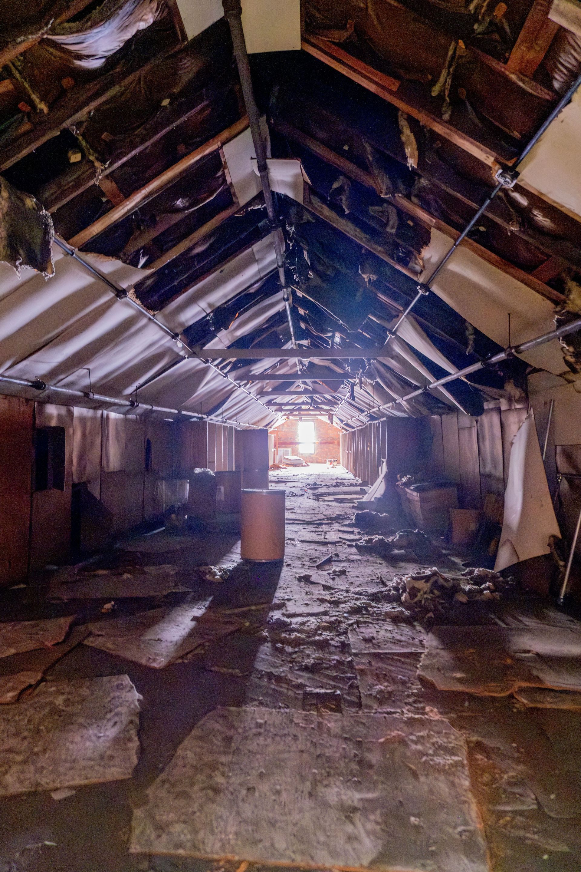 Damaged indoor hallway with collapsed ceiling, debris-strewn floor, and light at the far end