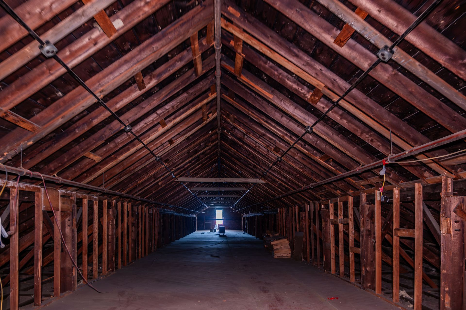Wooden attic with exposed rafters and a dark central aisle leading to bright light at the far end.