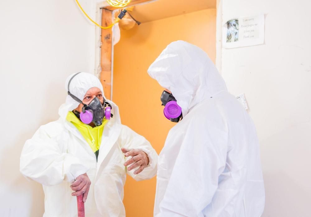 Two people wearing protective suits and masks are standing next to each other in a room.