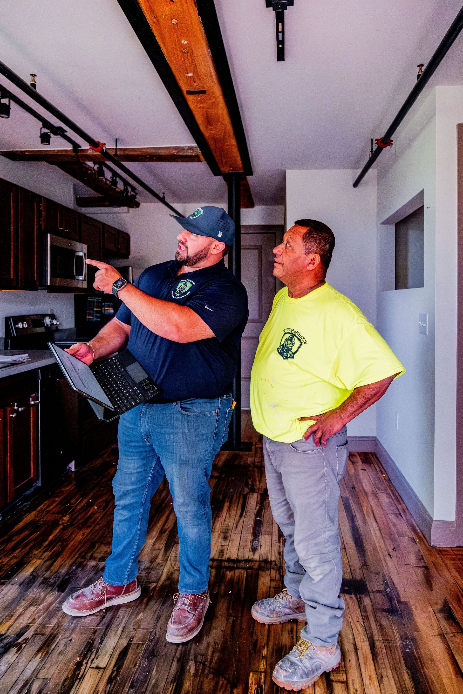 Two men in a utility room examining a wall-mounted system, one pointing while the other watches.