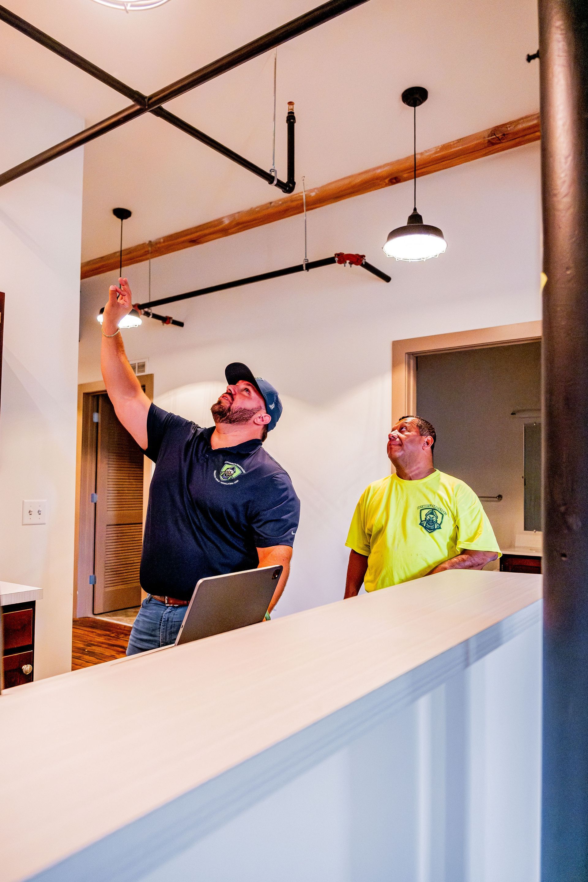 Two workers inspecting a ceiling in a bright room, one pointing upward while standing on a ladder.