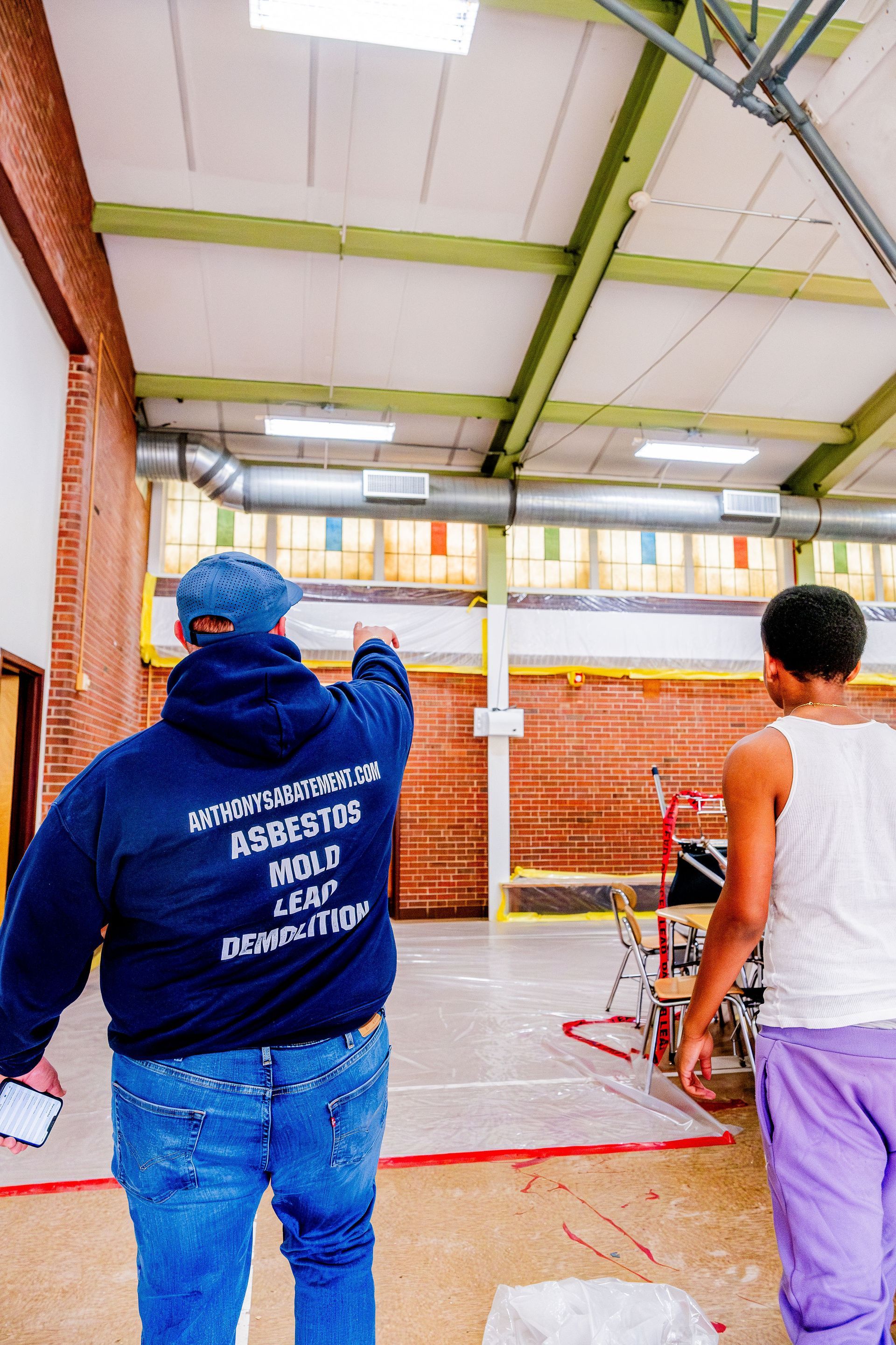 Two workers standing in a covered indoor area, one pointing ahead near brick walls and scaffolding.