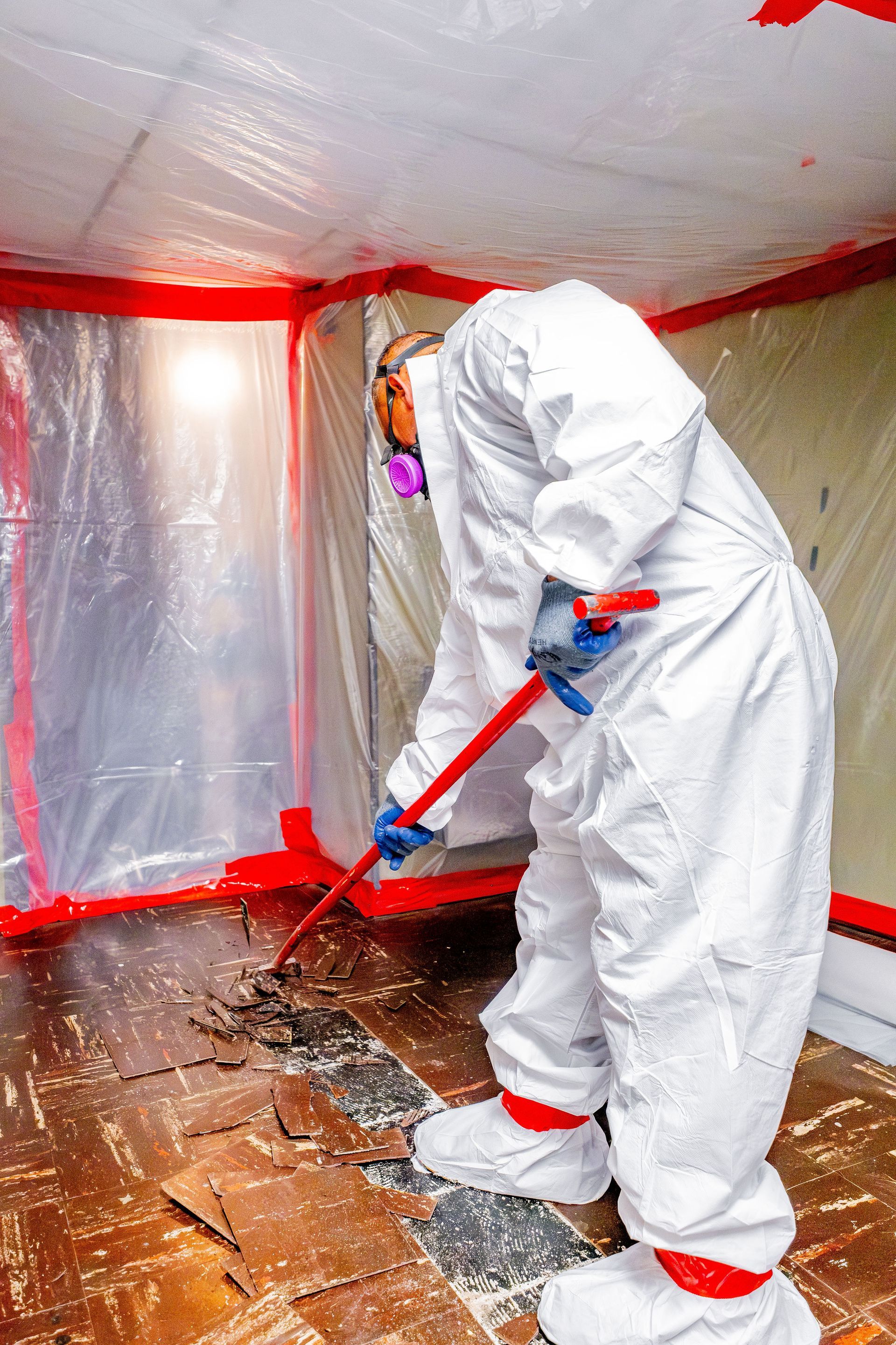 Person in white protective suit cleaning a room with a red mop inside a plastic-covered space