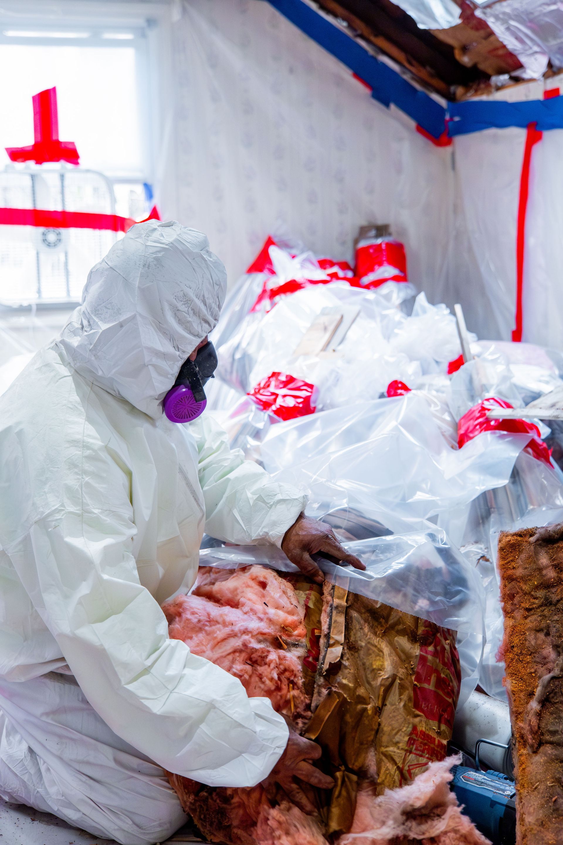 Person in white protective suit handling raw meat in a cold storage room with plastic-wrapped supplies.