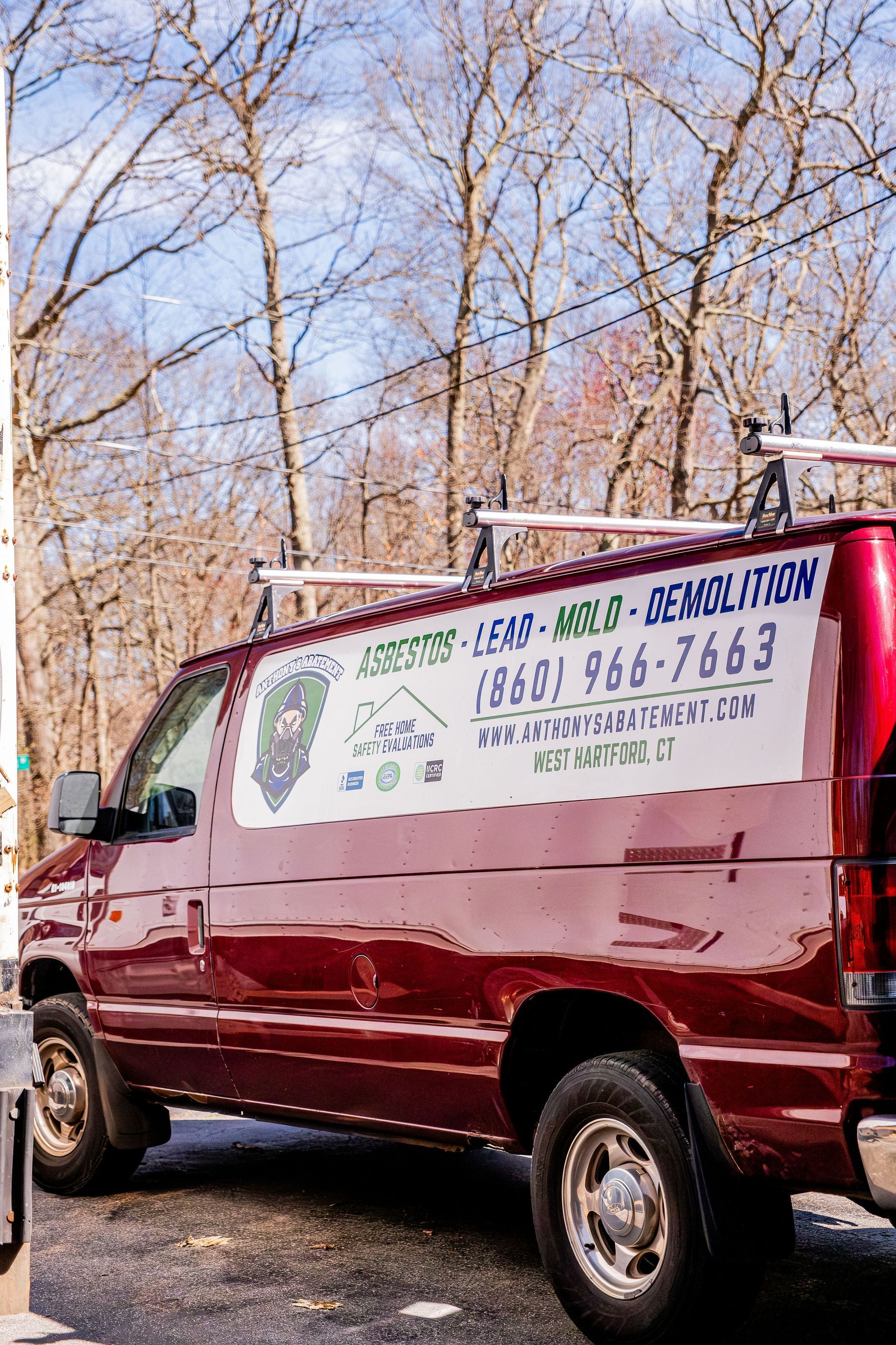 Maroon cargo van with a plumbing service sign parked by leafless trees